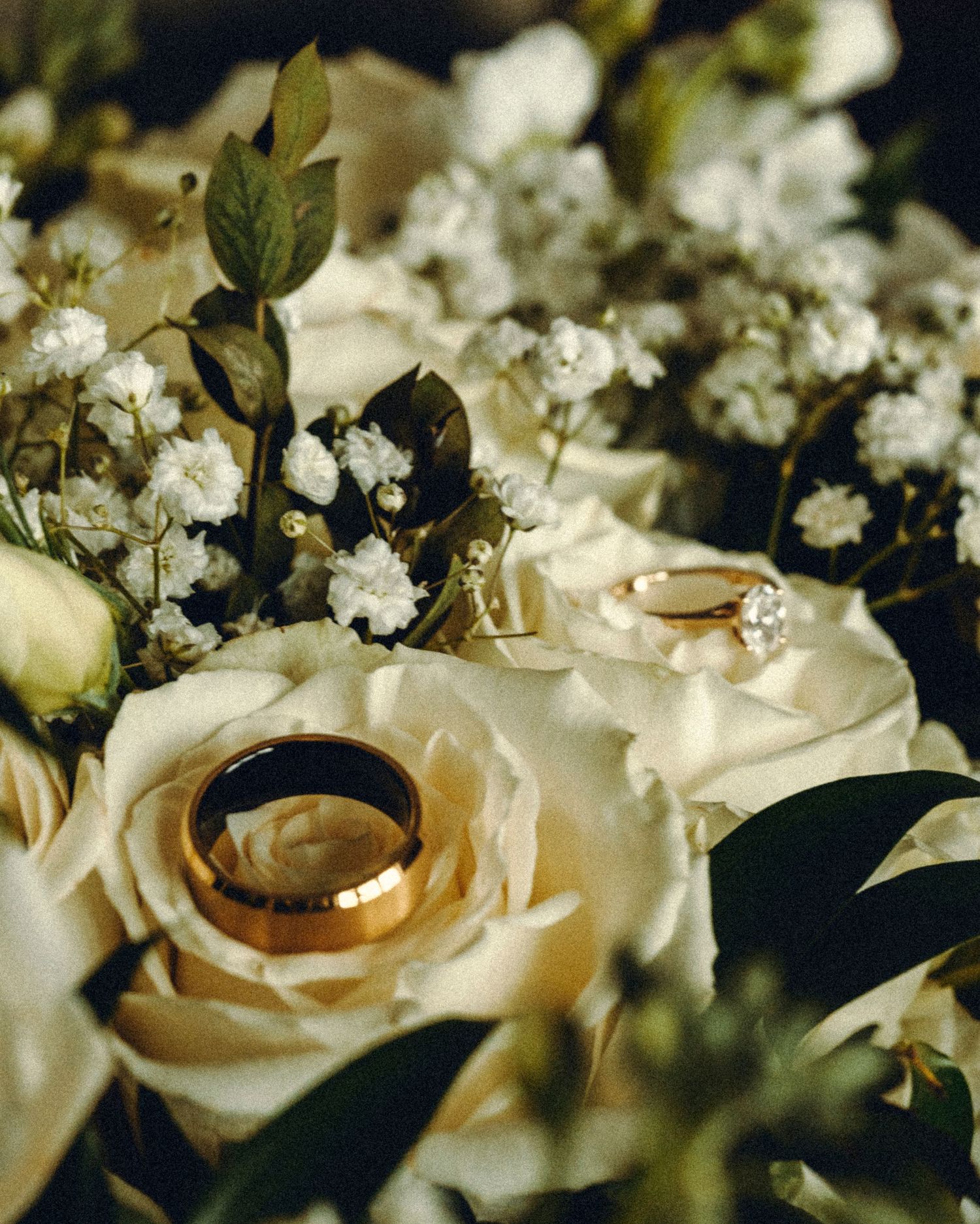 Two gold wedding bands rest elegantly among white roses and baby's breath in a bridal bouquet.