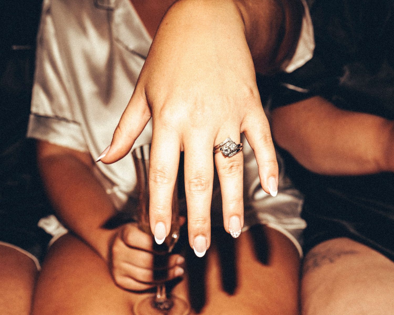 Close-up of bride's hand displaying large diamond engagement ring while holding champagne glass.