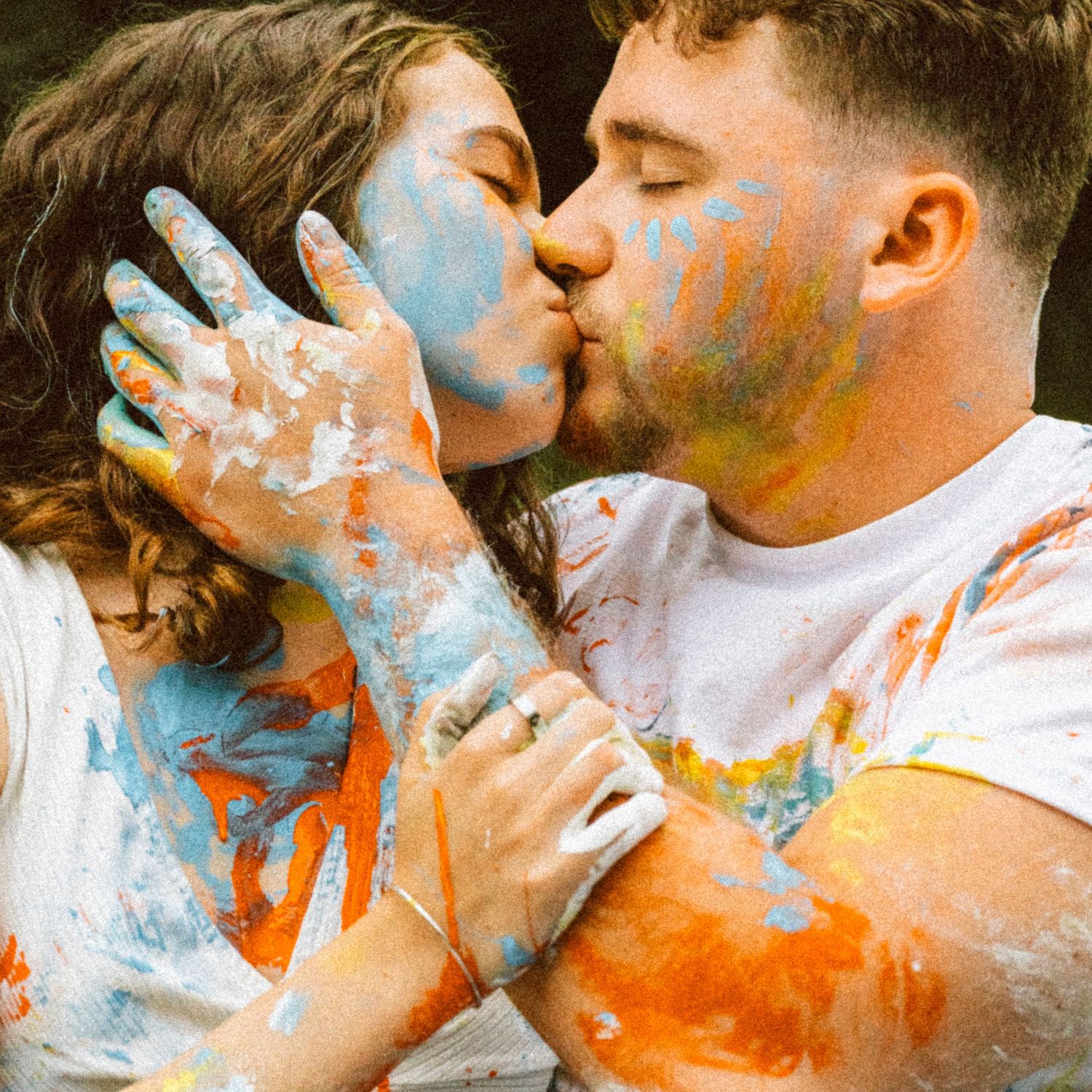 Couple kissing covered in colorful paint during a fun engagement photo shoot.