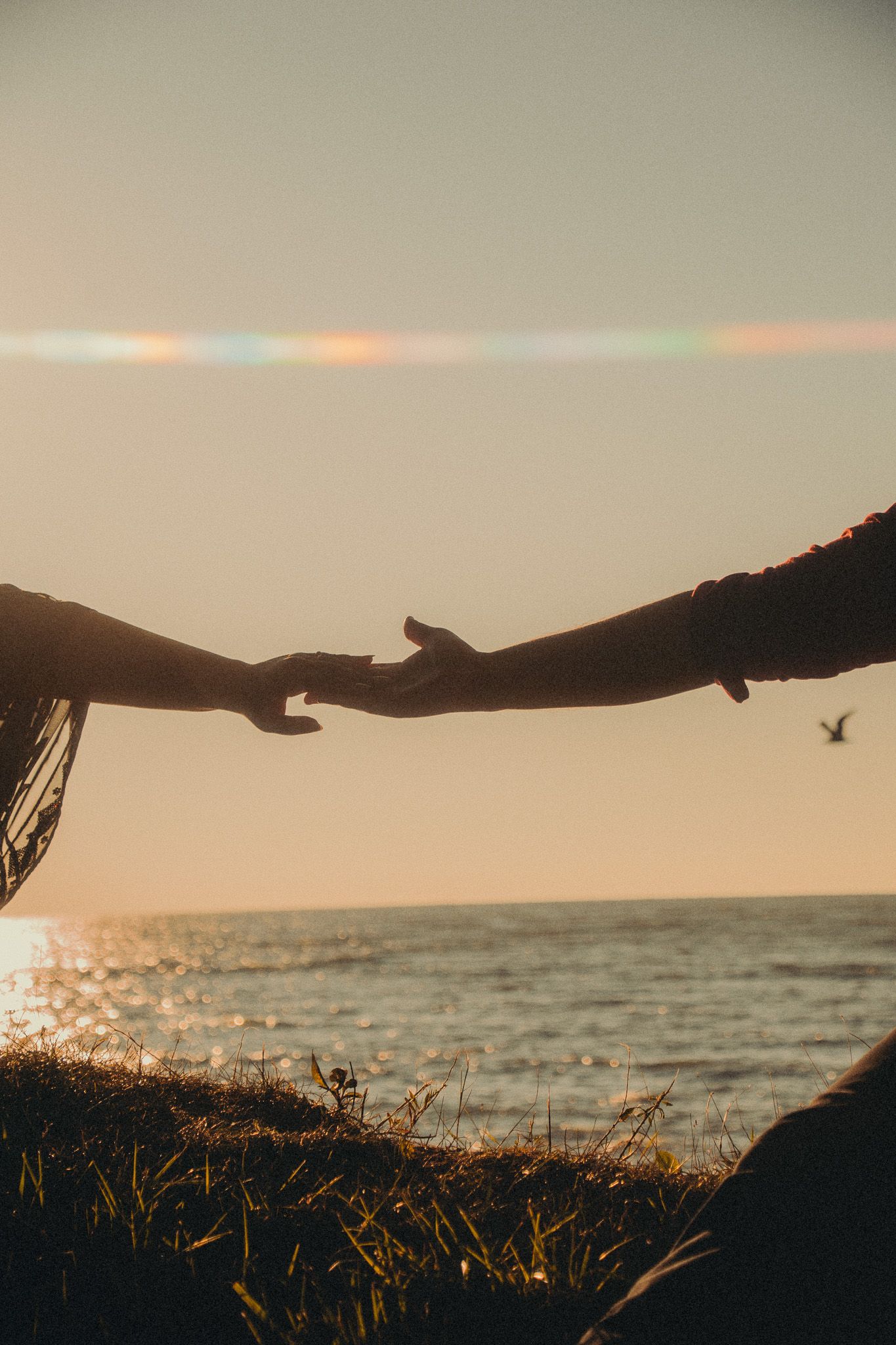Two hands reaching toward each other against a golden ocean sunset sky.