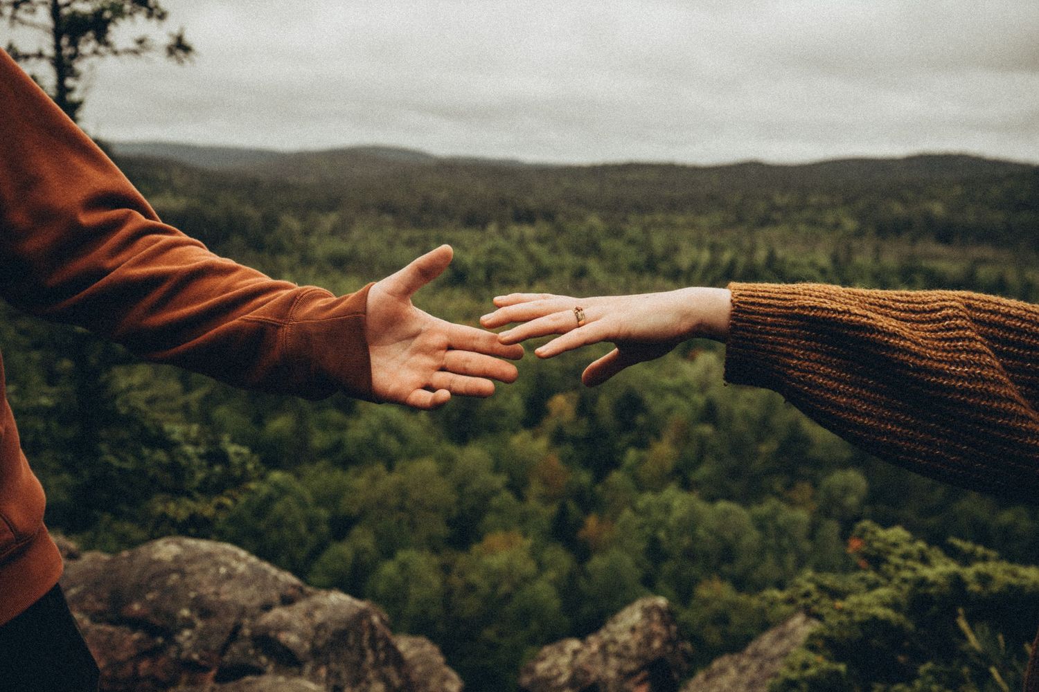 A couple reaching out to hold hands with a scenic forest valley in background.