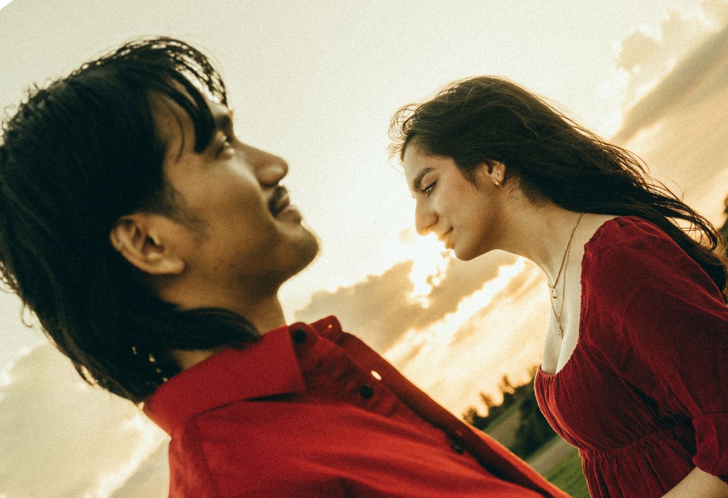 Romantic couple in red shirts gazing at each other during golden hour.