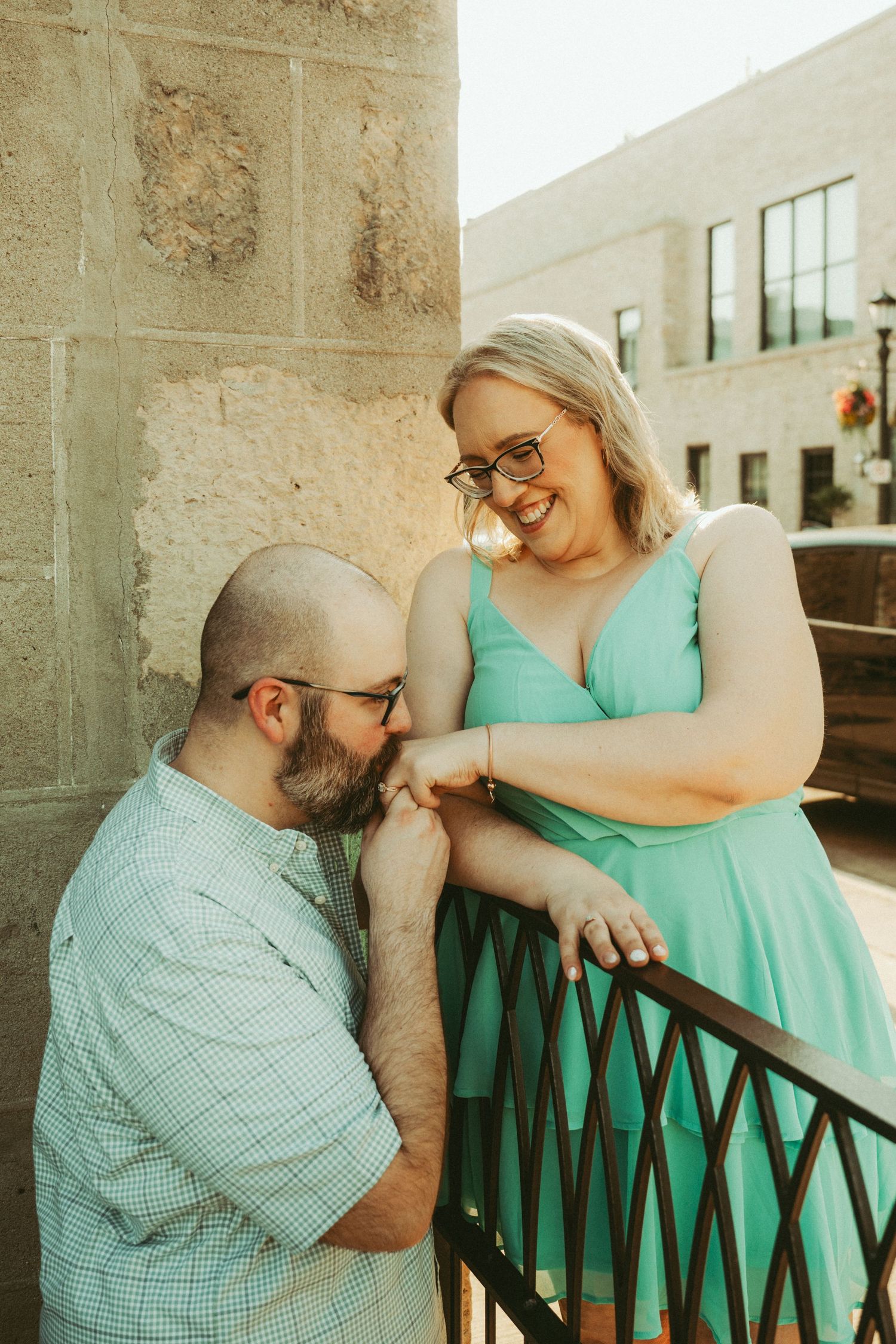 Happy couple sharing a tender moment on a balcony, woman in mint green dress laughing with bearded man.