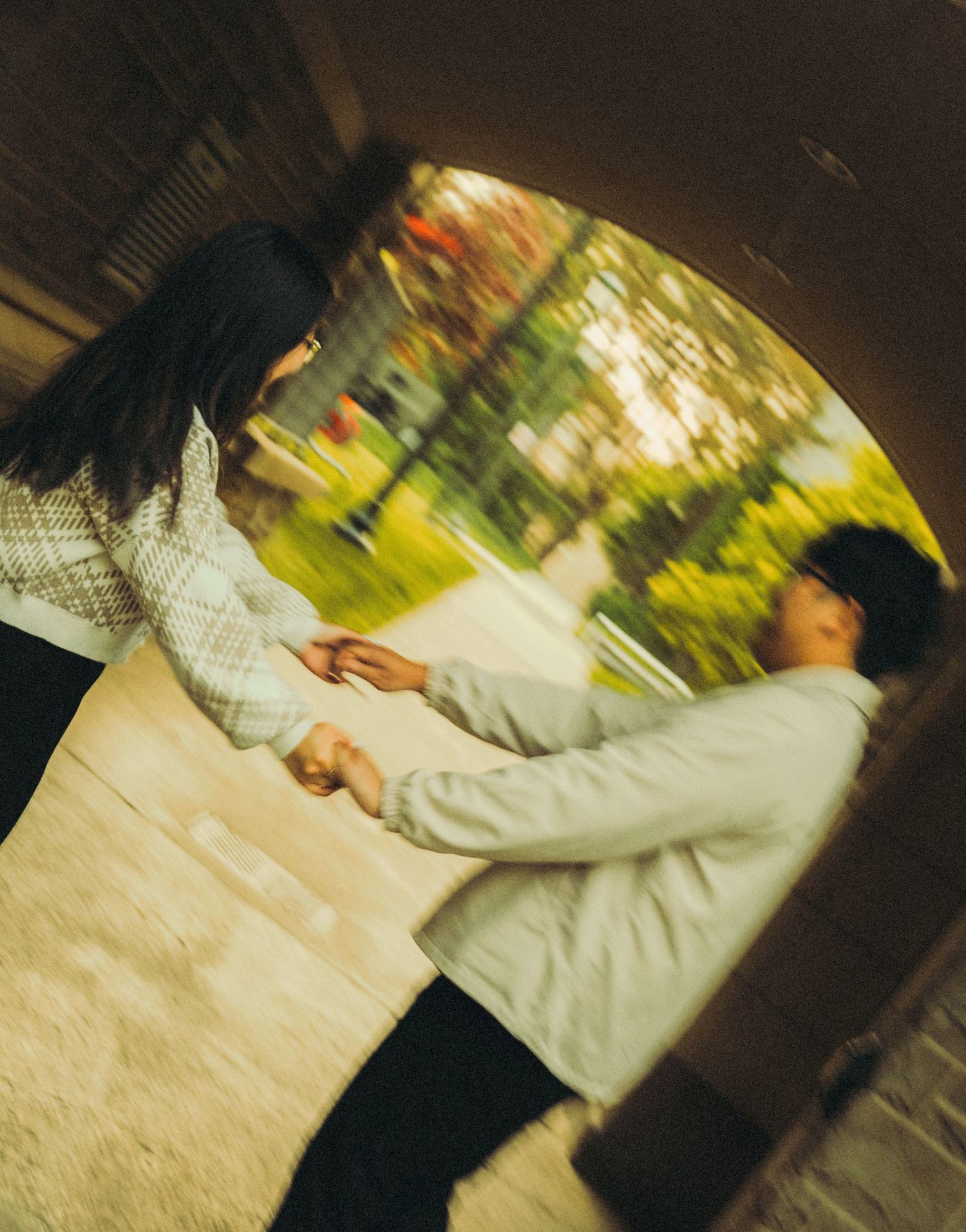 Couple holding hands tenderly in a circular tunnel archway with a blurred garden background.