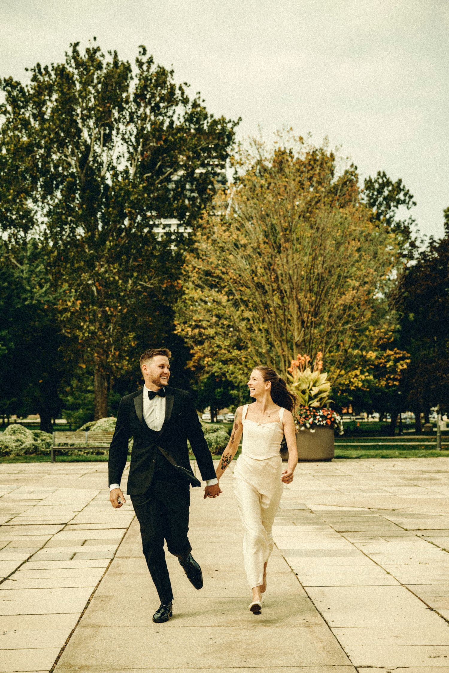Bride and groom holding hands and walking through a park on their wedding day.