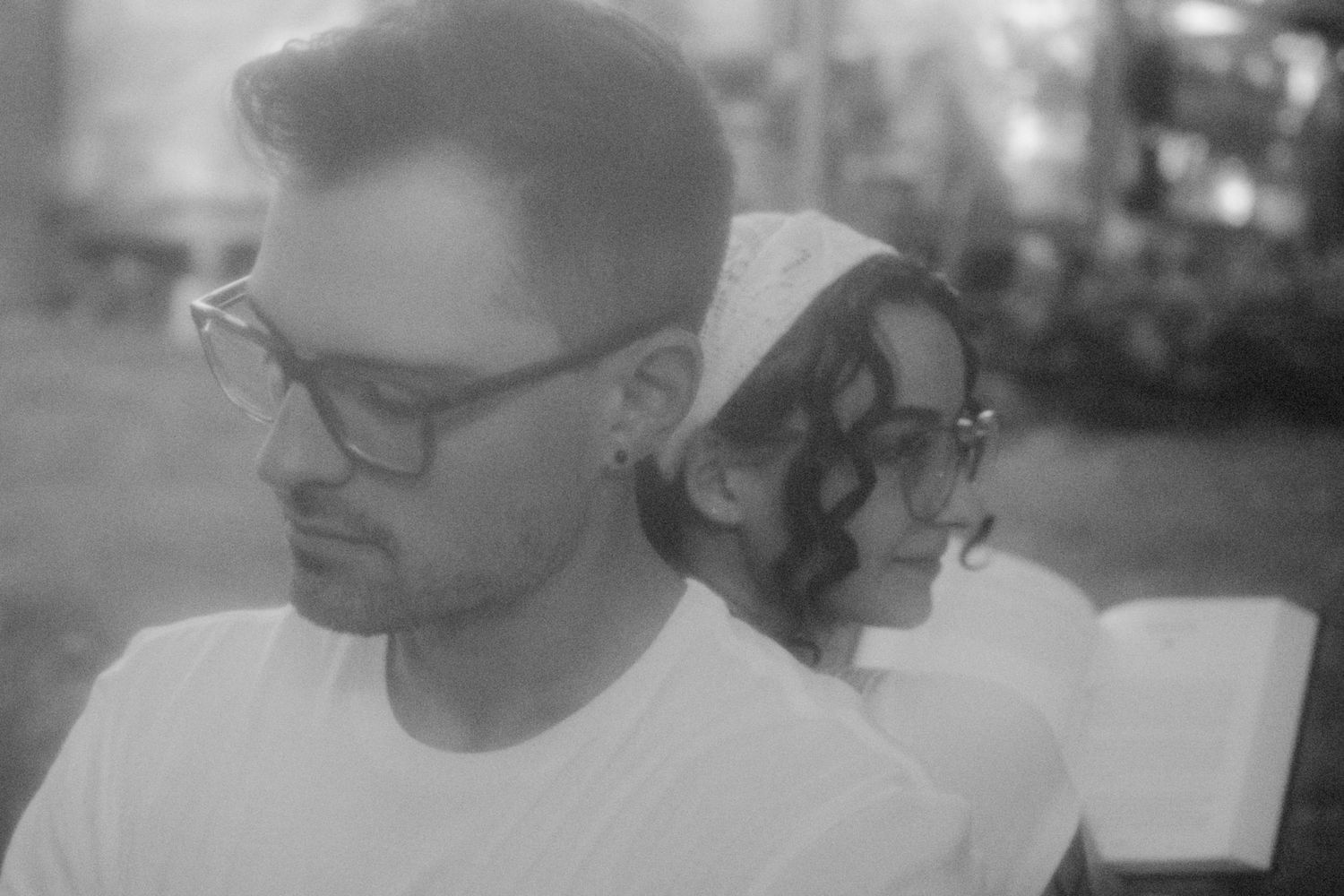Black and white portrait of a man and woman sitting back to back outdoors.