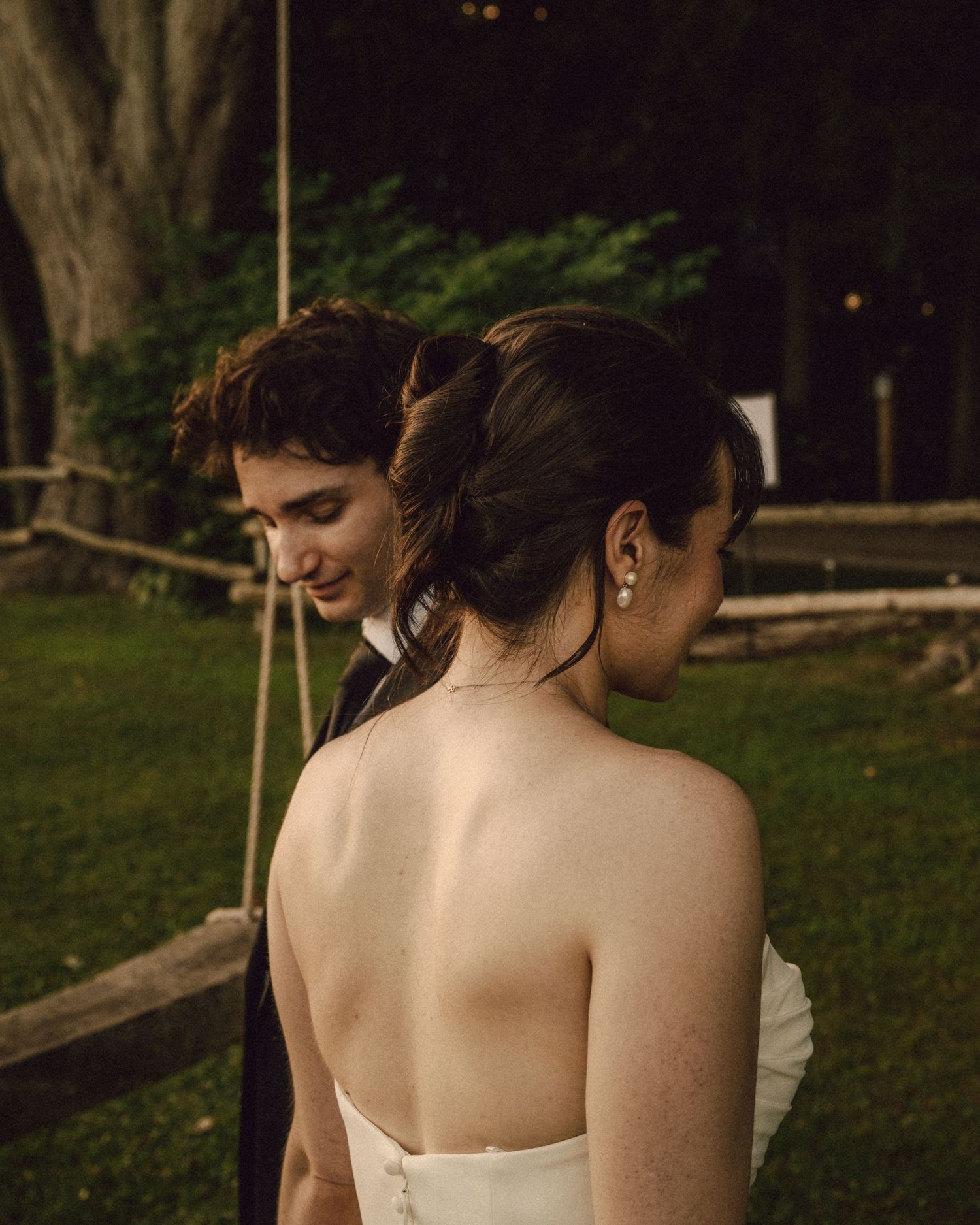Intimate close-up of bride and groom in soft evening light outdoors near a rustic wooden fence.