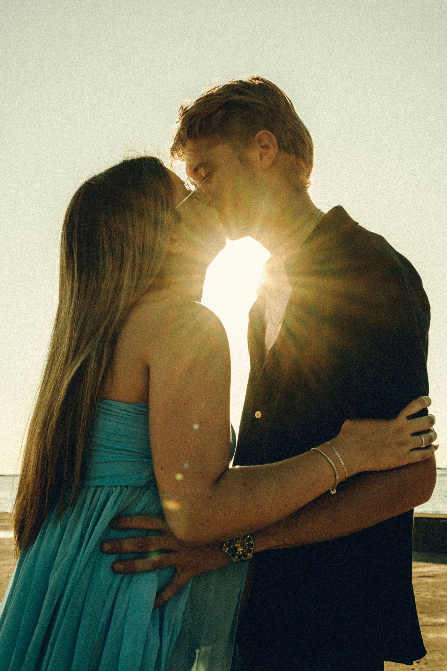 Romantic couple kissing at sunset on the beach with golden sun flare glowing between them.