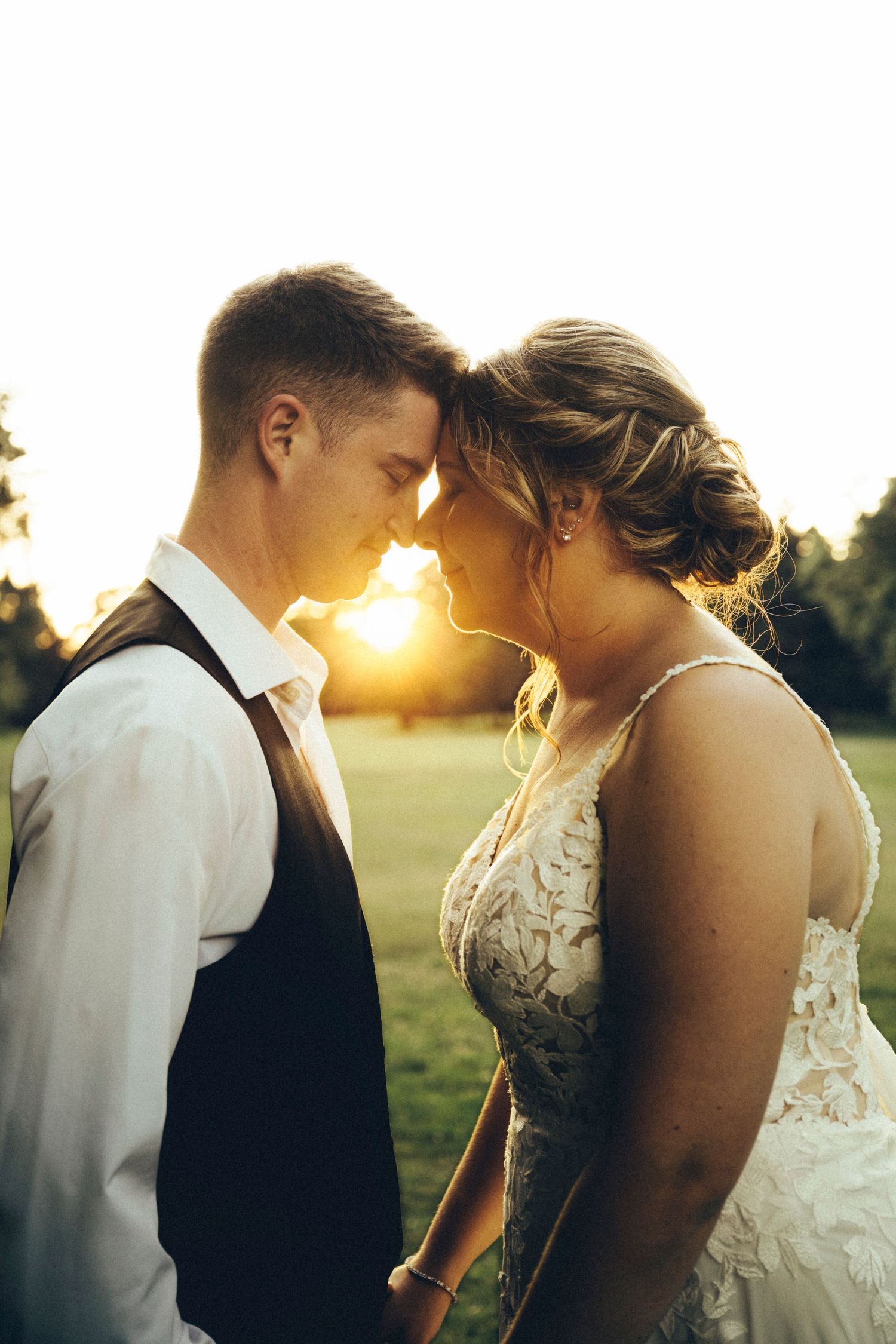 Bride and groom touch foreheads tenderly in golden sunset light on wedding day.