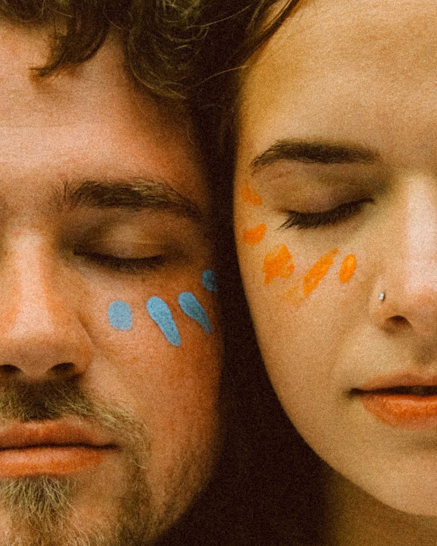 Close-up of couple with eyes closed, blue and orange paint strokes on their cheeks.