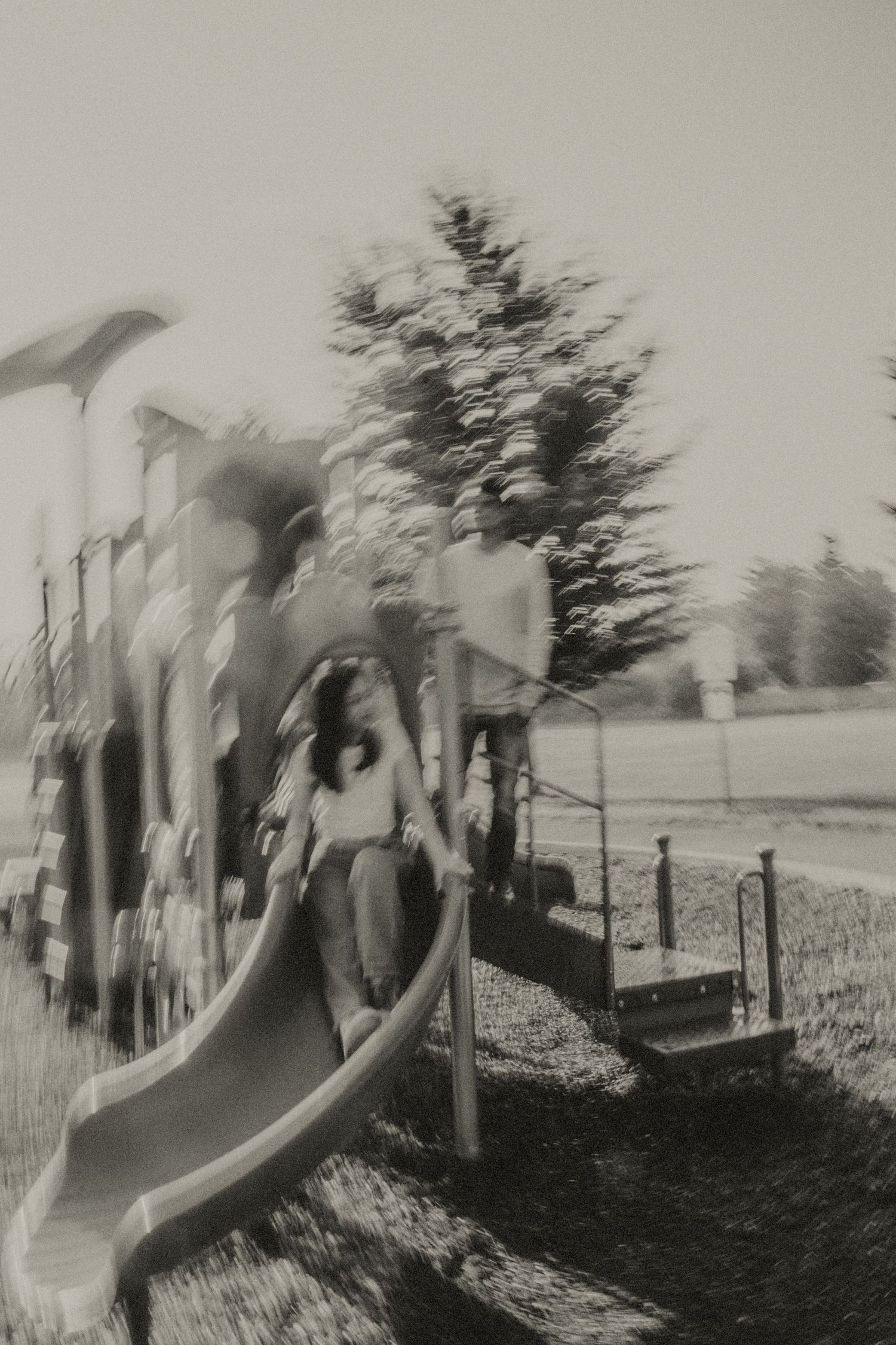 A vintage black and white photo captures children playing on a playground slide with dreamy motion blur.