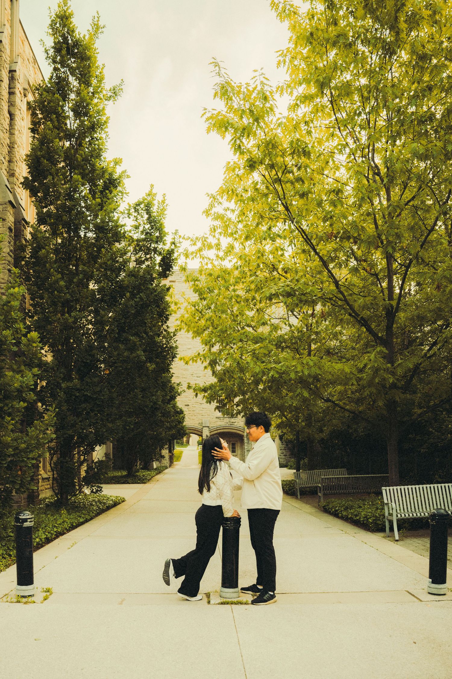 Couple dancing playfully on a tree-lined campus walkway in warm autumn light.
