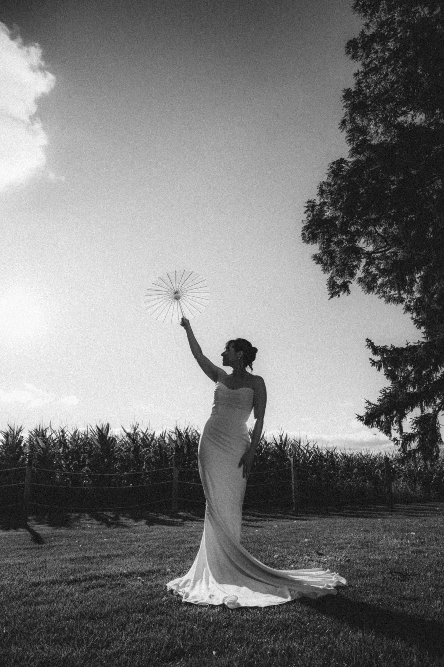 Bride in white gown holding fan aloft in black and white silhouette.