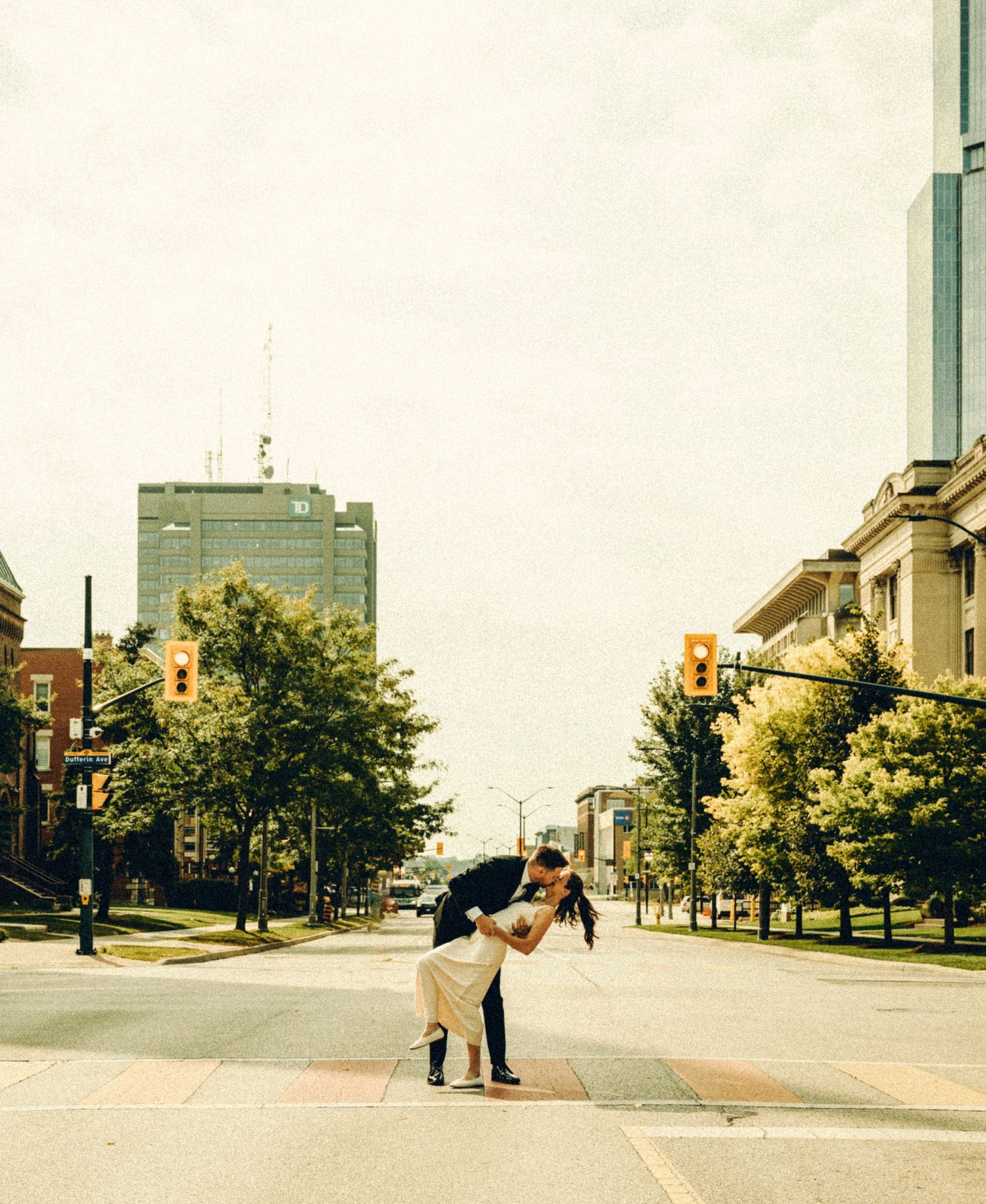Couple shares romantic dip kiss in middle of urban street with city buildings and trees.