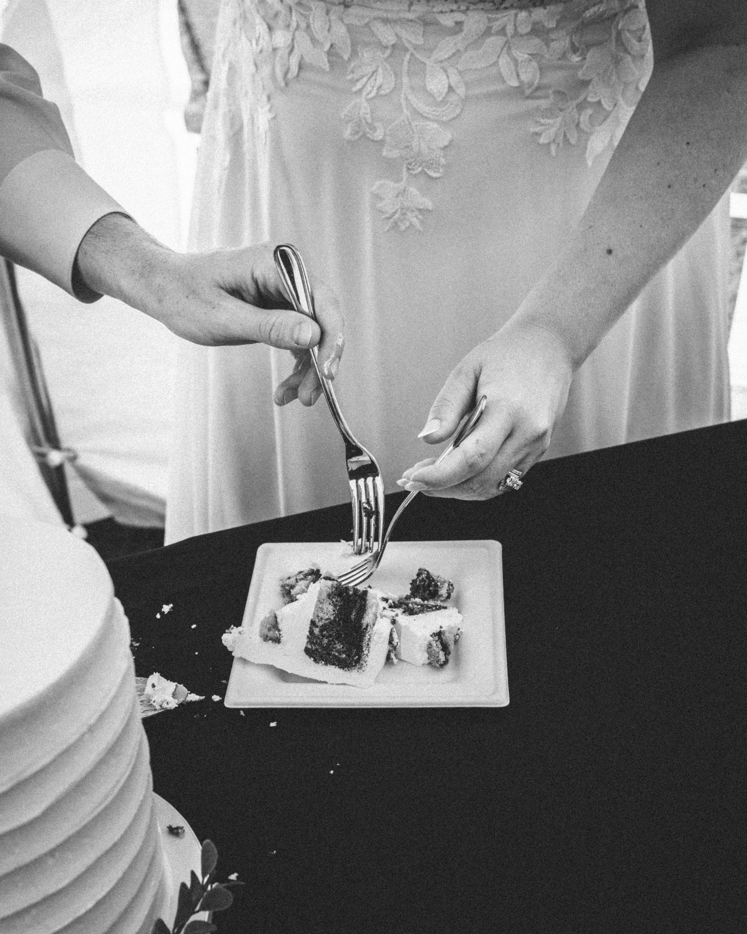 Bride and groom cut wedding cake together in black and white close-up photo.