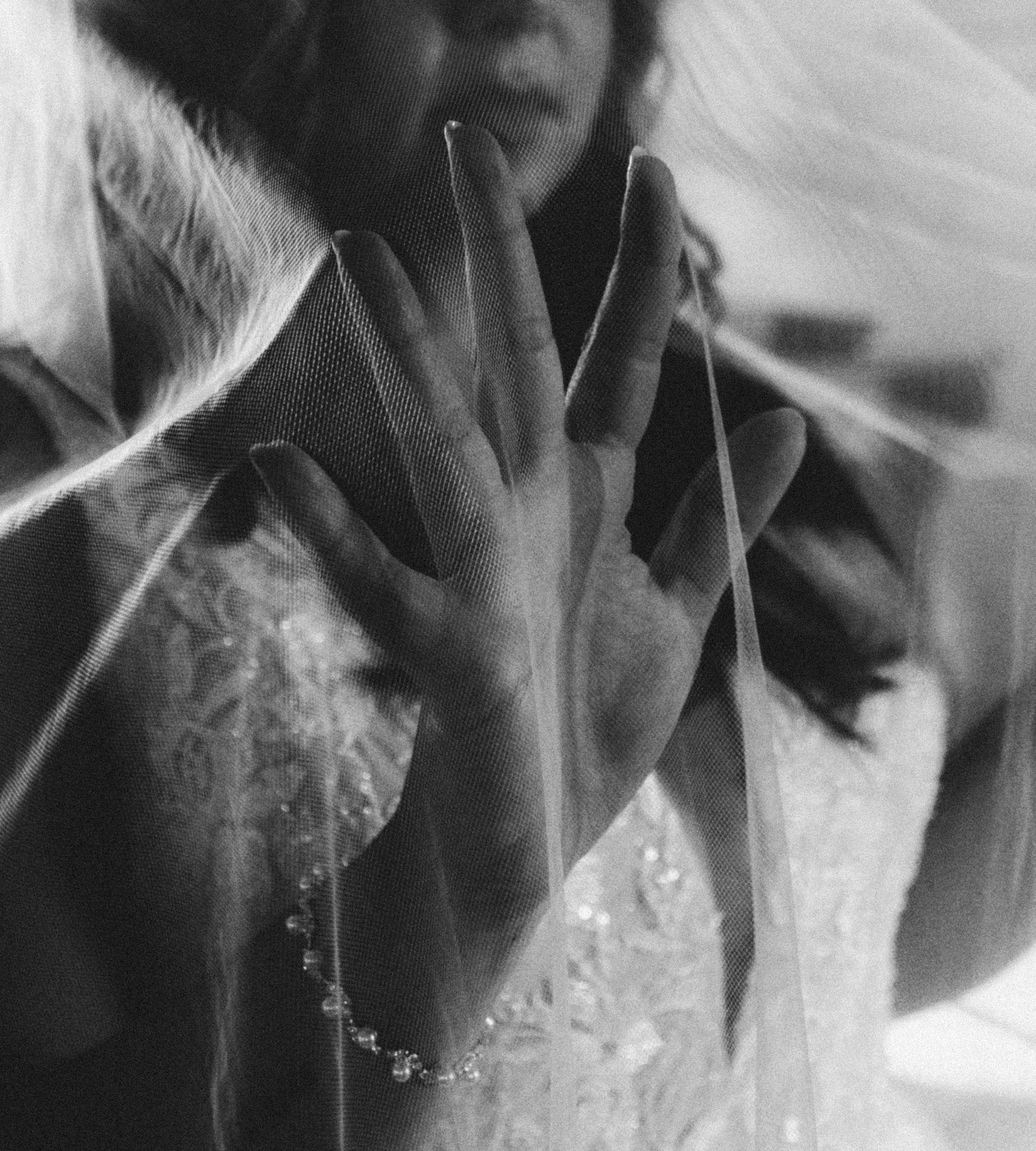 Black and white close-up of bride's hand with pearl bracelet through wedding veil.