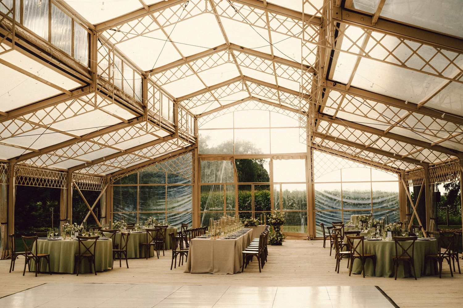 Stunning glass greenhouse wedding reception venue with latticed roof, green draped tables and panoramic garden views.