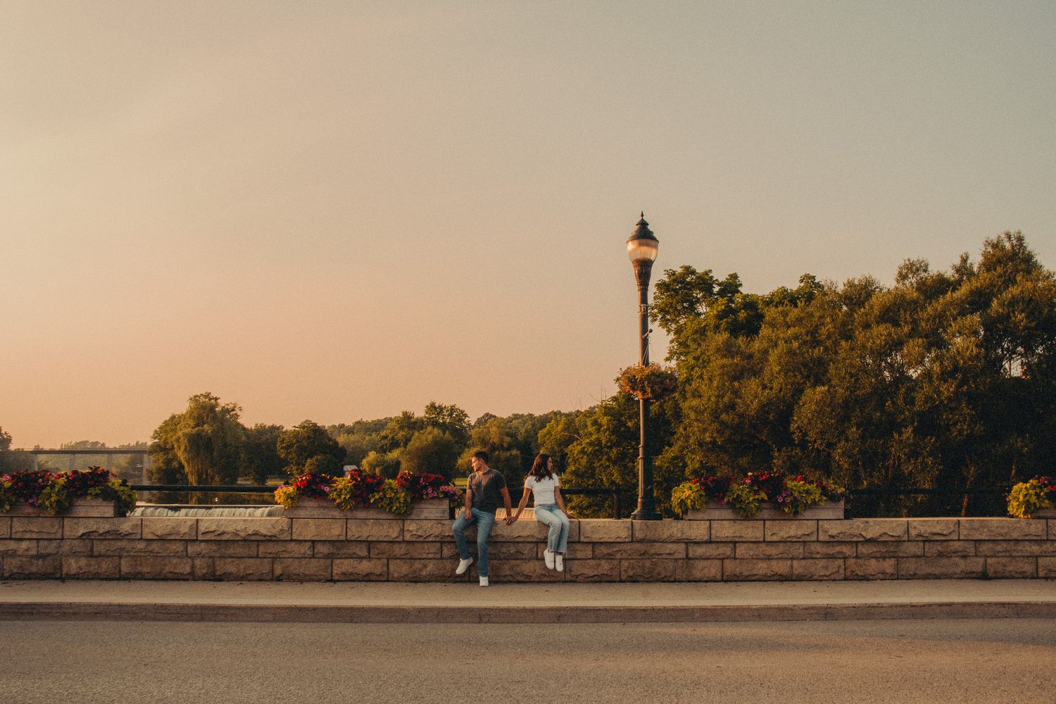 Couple leaning against stone wall by bridge at golden hour sunset.