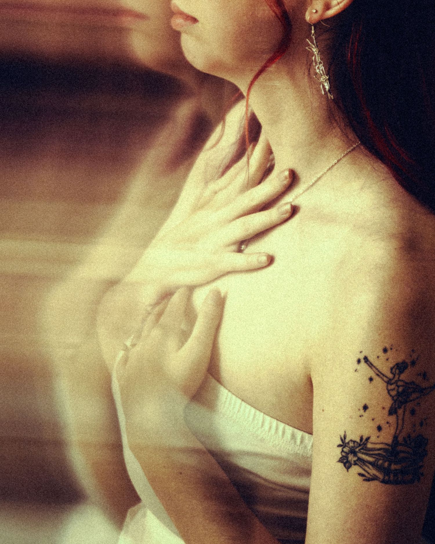 Close-up of woman in white dress with star tattoo on shoulder holding hand to chest.