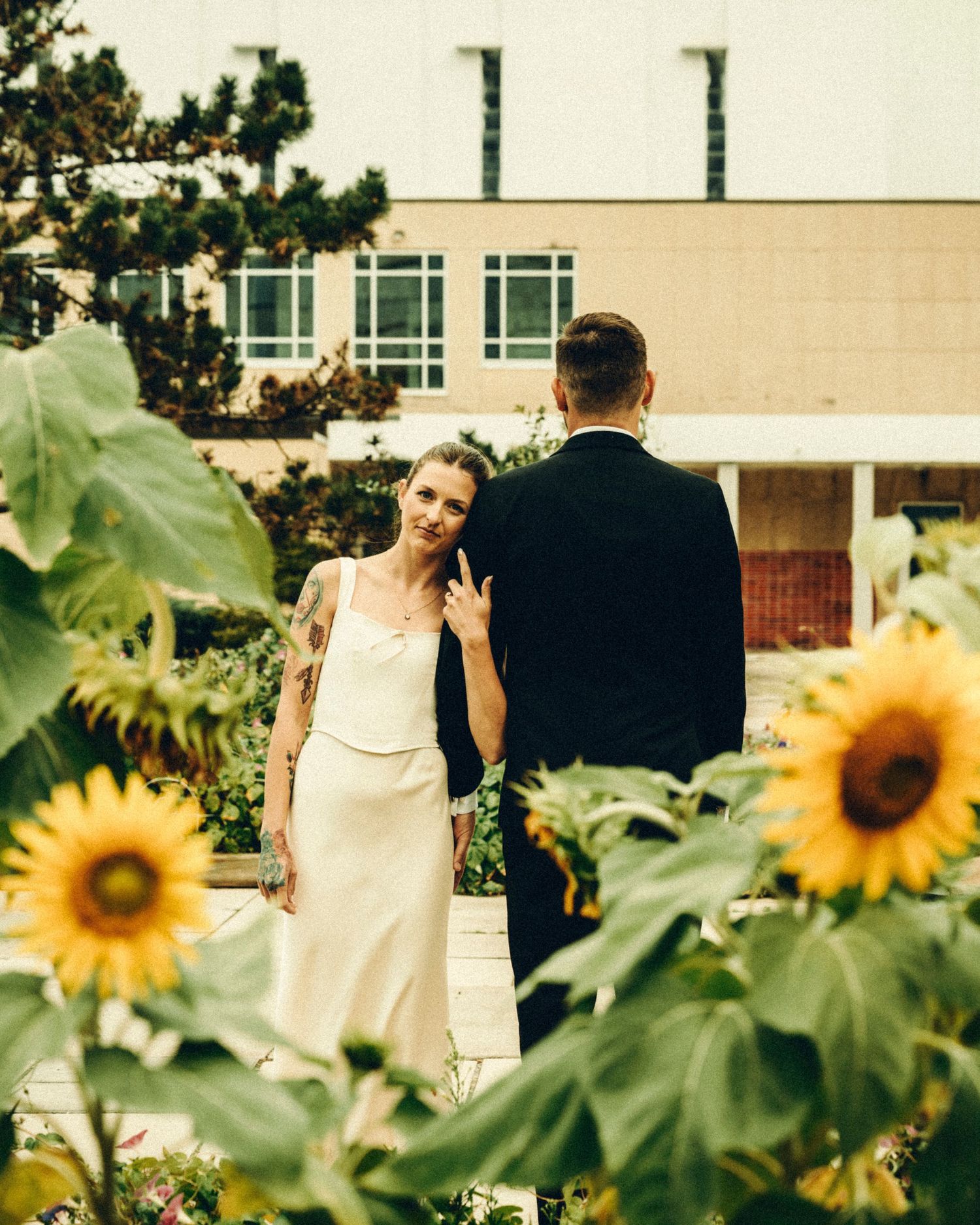 Bride in white dress smiling at groom among sunflowers in a garden during outdoor wedding.