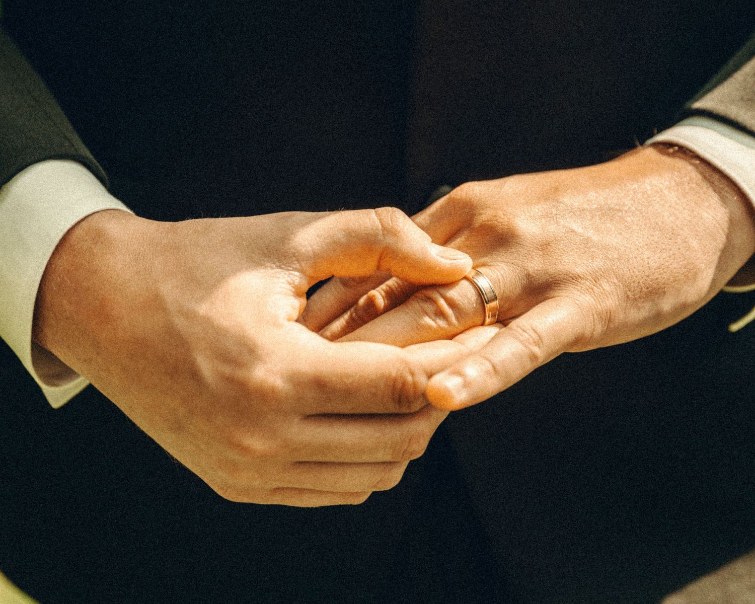Close-up of groom placing wedding band on finger during wedding ring exchange ceremony.
