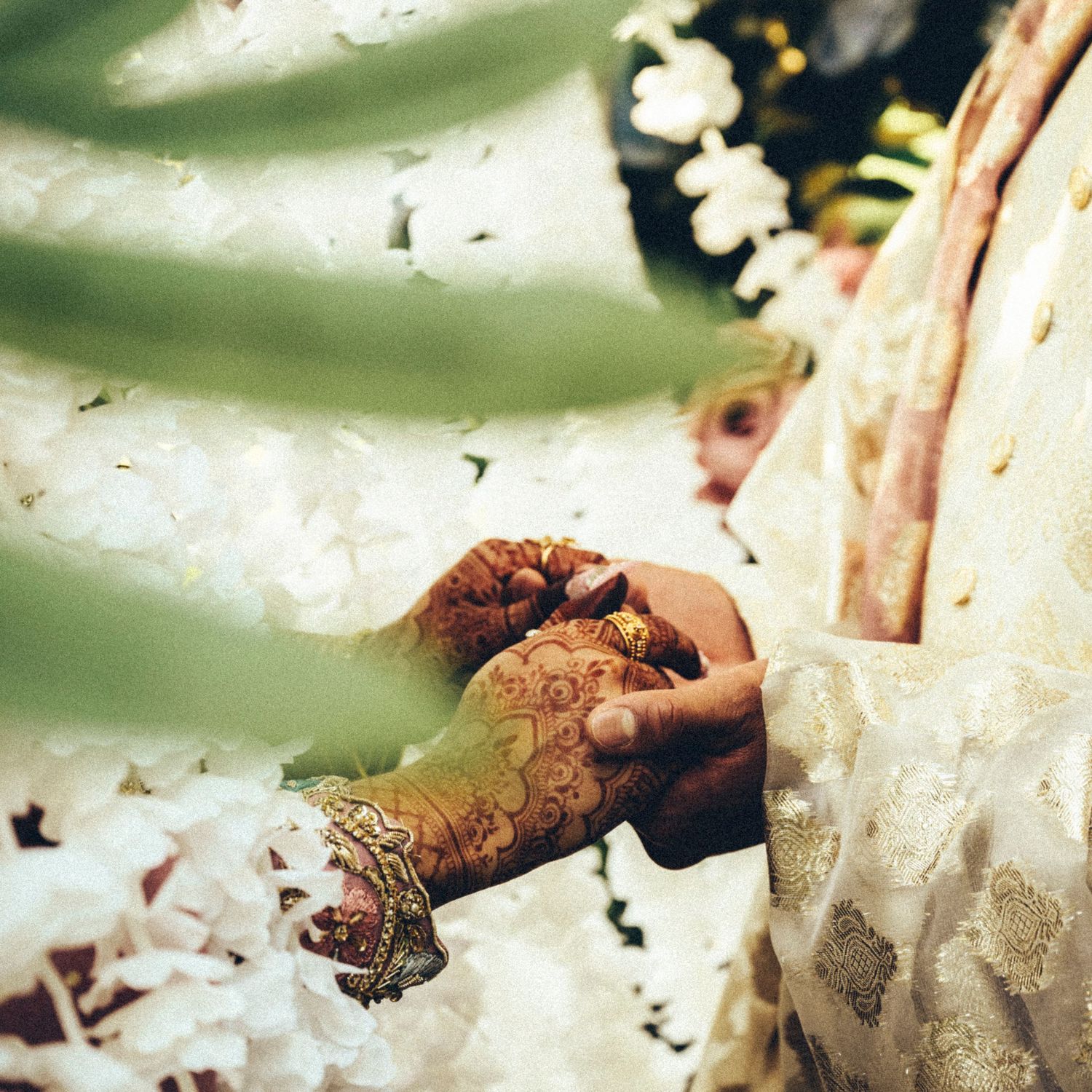 Close-up of South Asian wedding ceremony with henna-adorned bride's hands surrounded by white floral garlands.