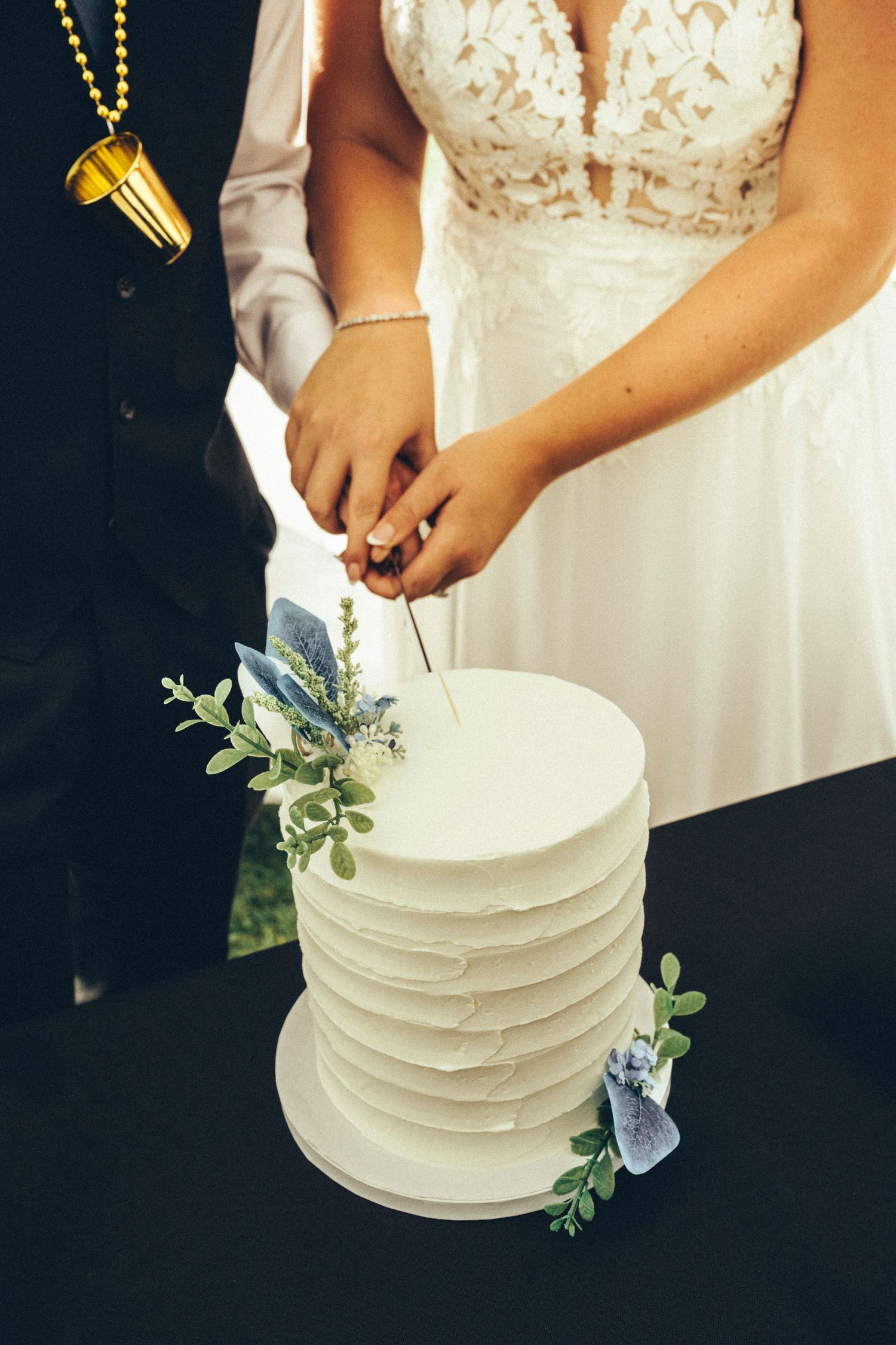 Bride and groom cut elegant white textured wedding cake decorated with blue flowers and greenery.