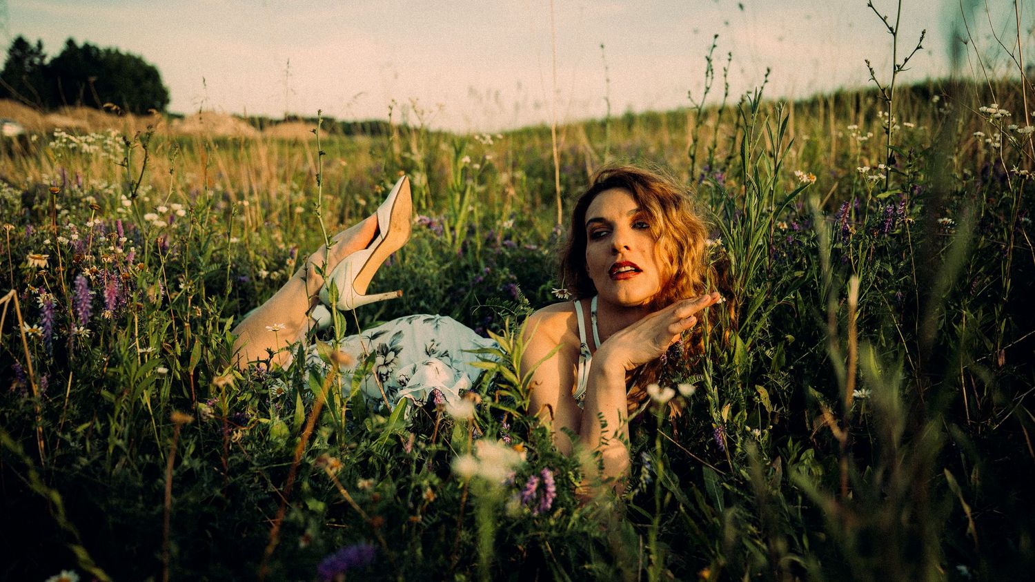 Woman in floral dress lying in wildflower meadow at golden hour sunset.