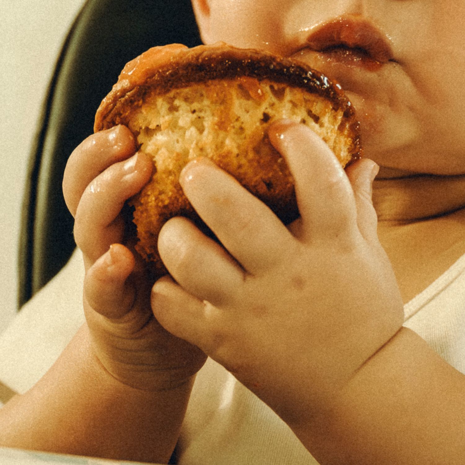 Close-up of baby hands holding a muffin up to their mouth.