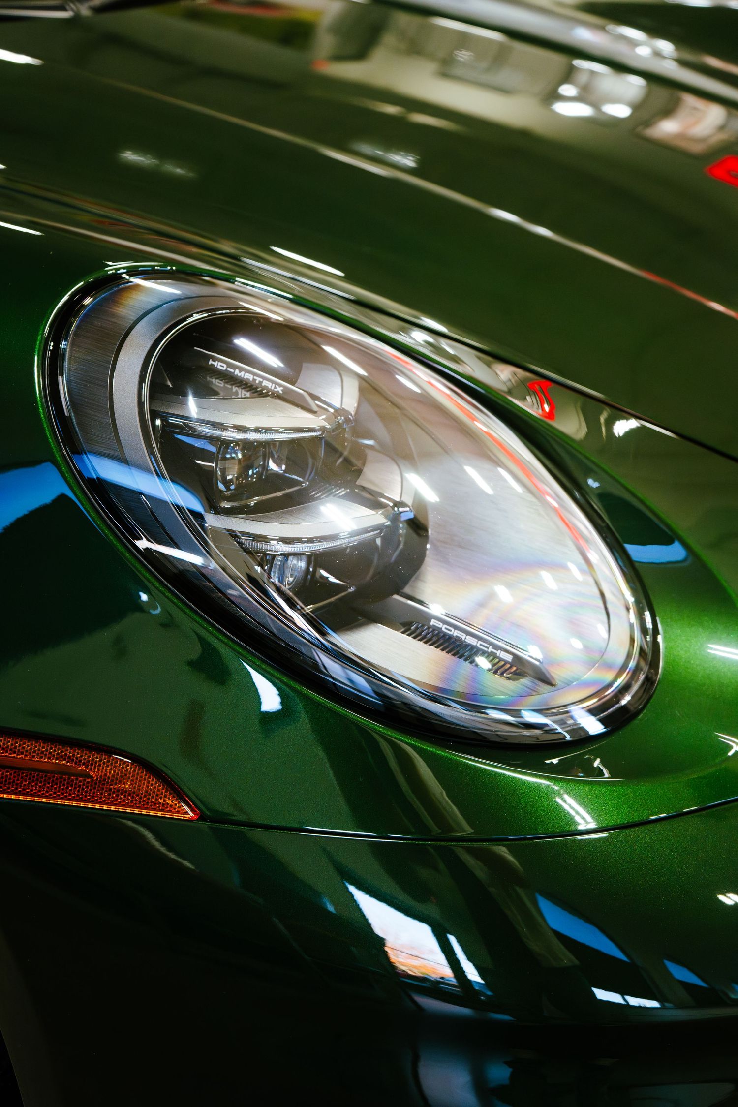 Close-up of a green Porsche 911 headlight with chrome detailing and LED daytime running lights.
