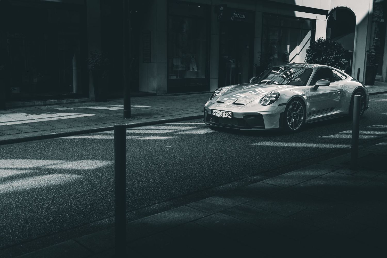 Silver Porsche 911 GT3 driving through a quiet urban street in black and white.