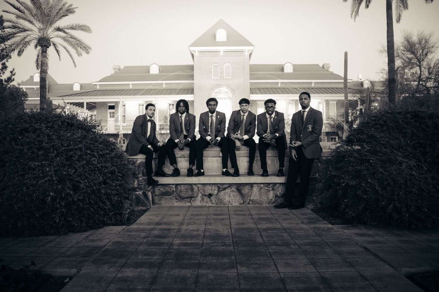 Black and white photo of seven young men in suits sitting on a fountain wall at the University of Arizona.
