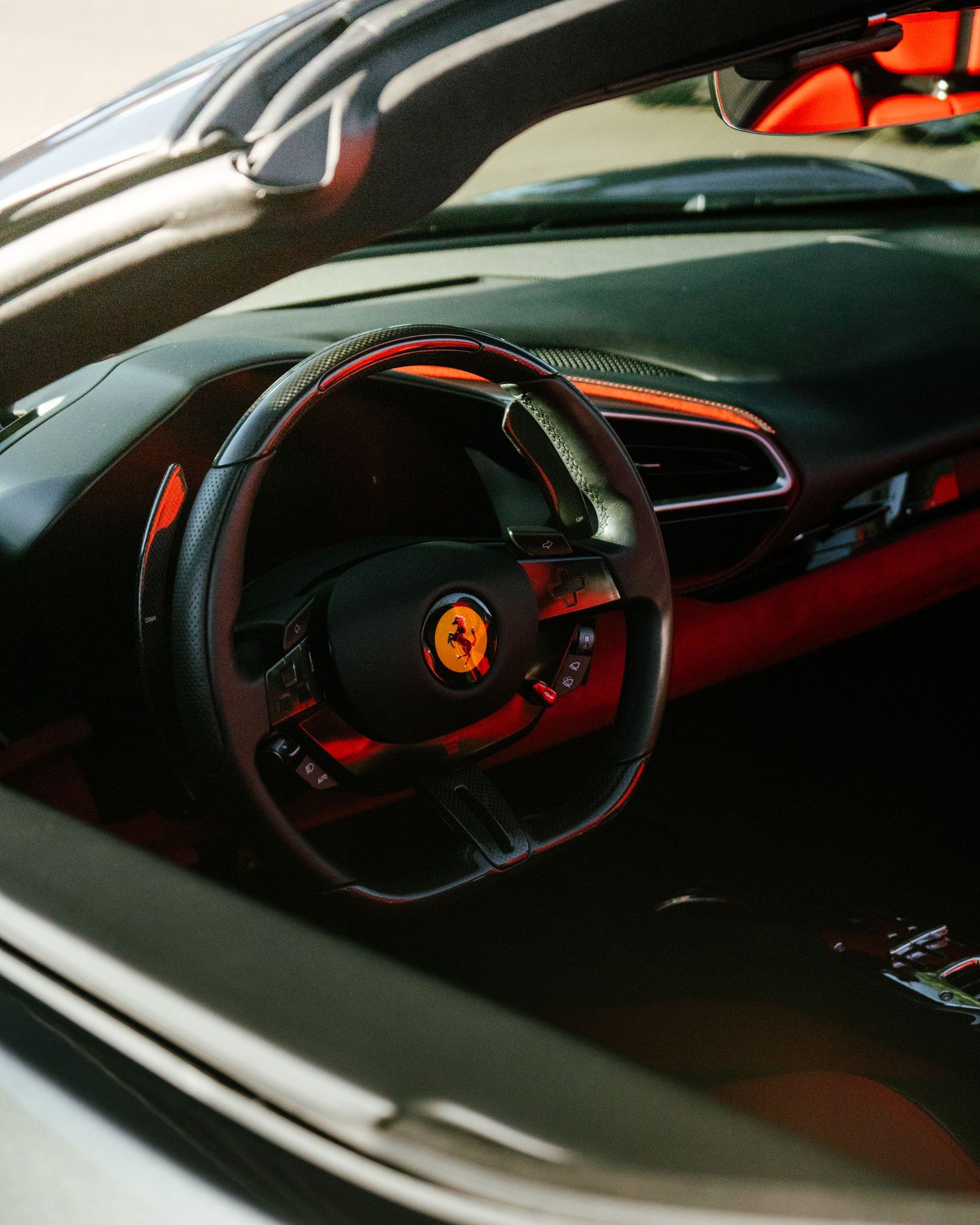 Ferrari sports car interior featuring a black and red leather steering wheel with iconic prancing horse logo and vibrant red accents.