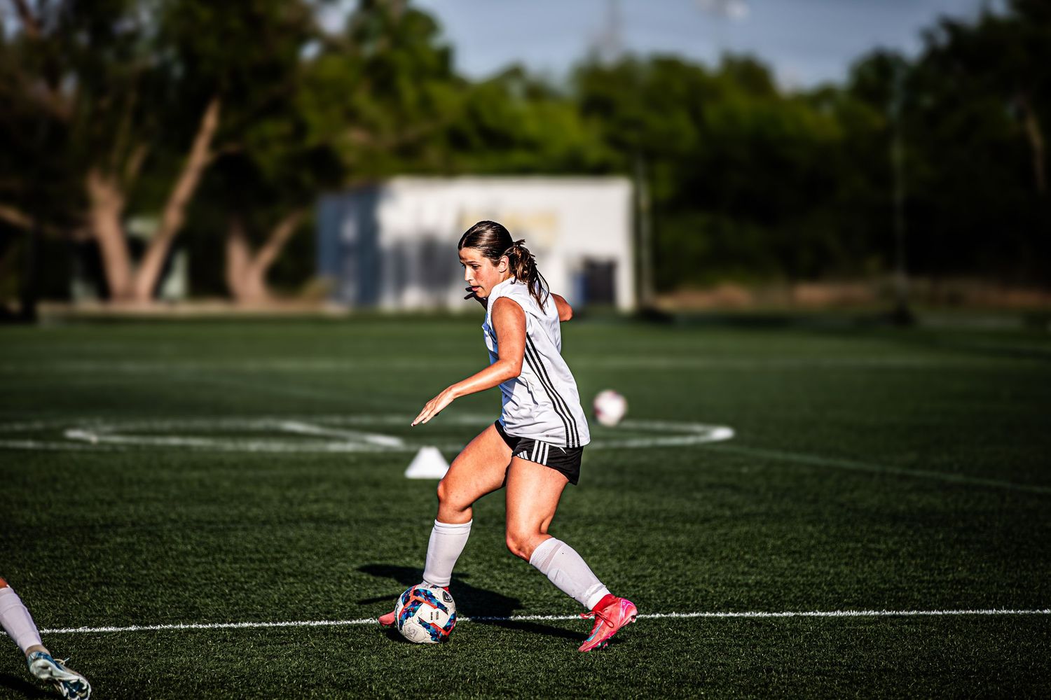 Soccer player dribbles ball across sunny sports field during practice.