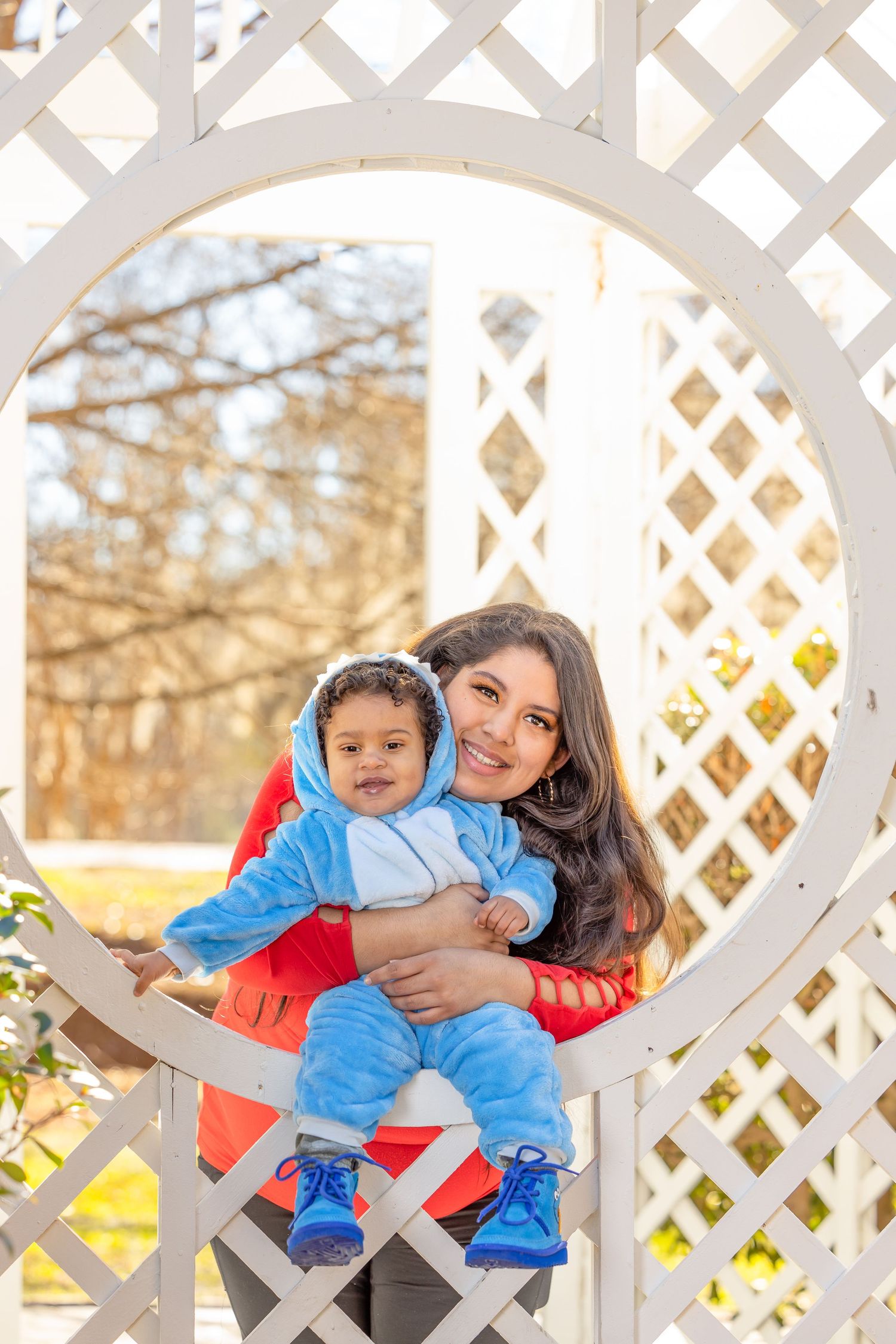 Parent and child share playful moment in front of decorative white lattice garden structure.