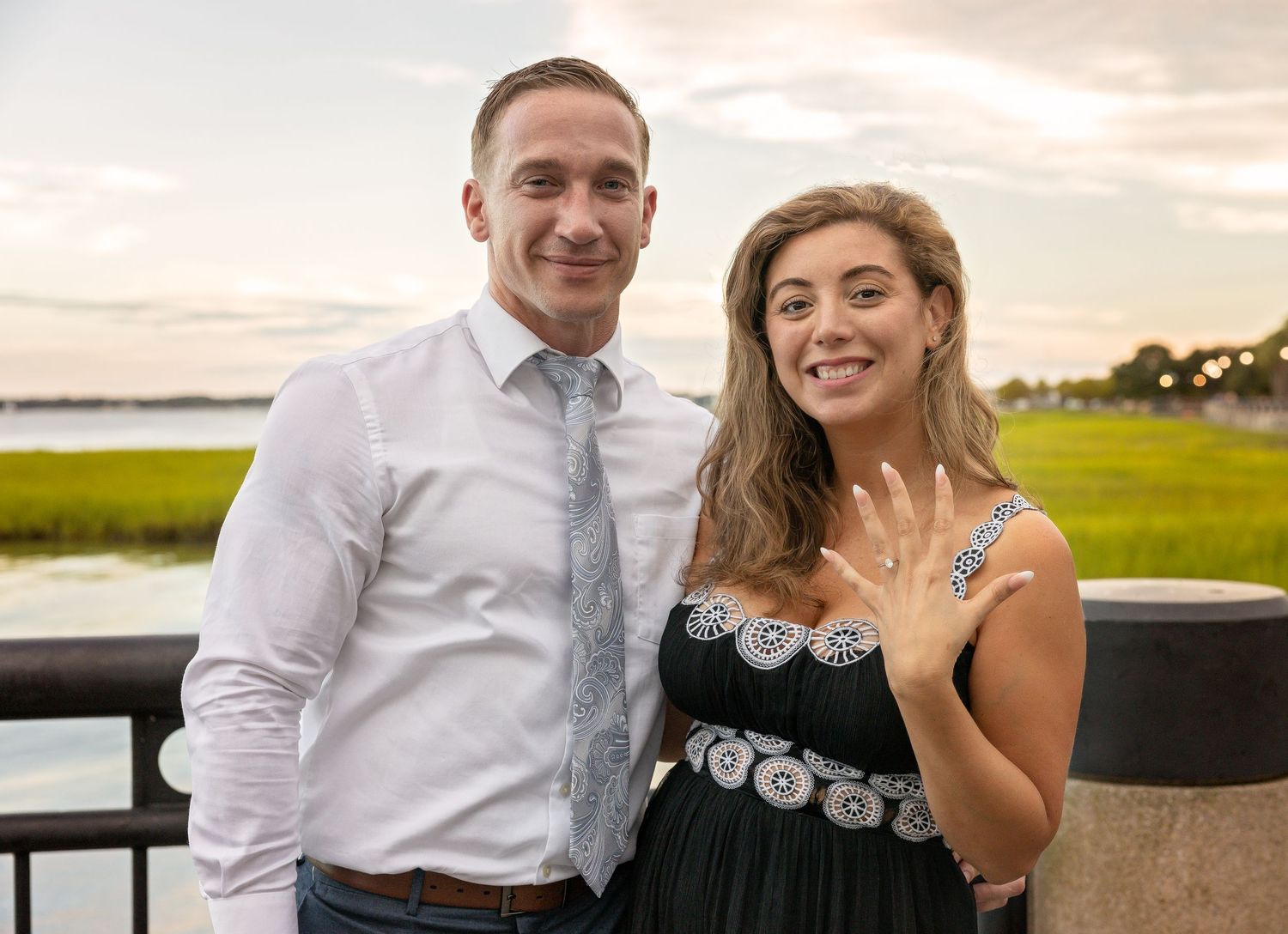 Couple shares romantic moment at sunset by waterfront with dramatic orange sky.