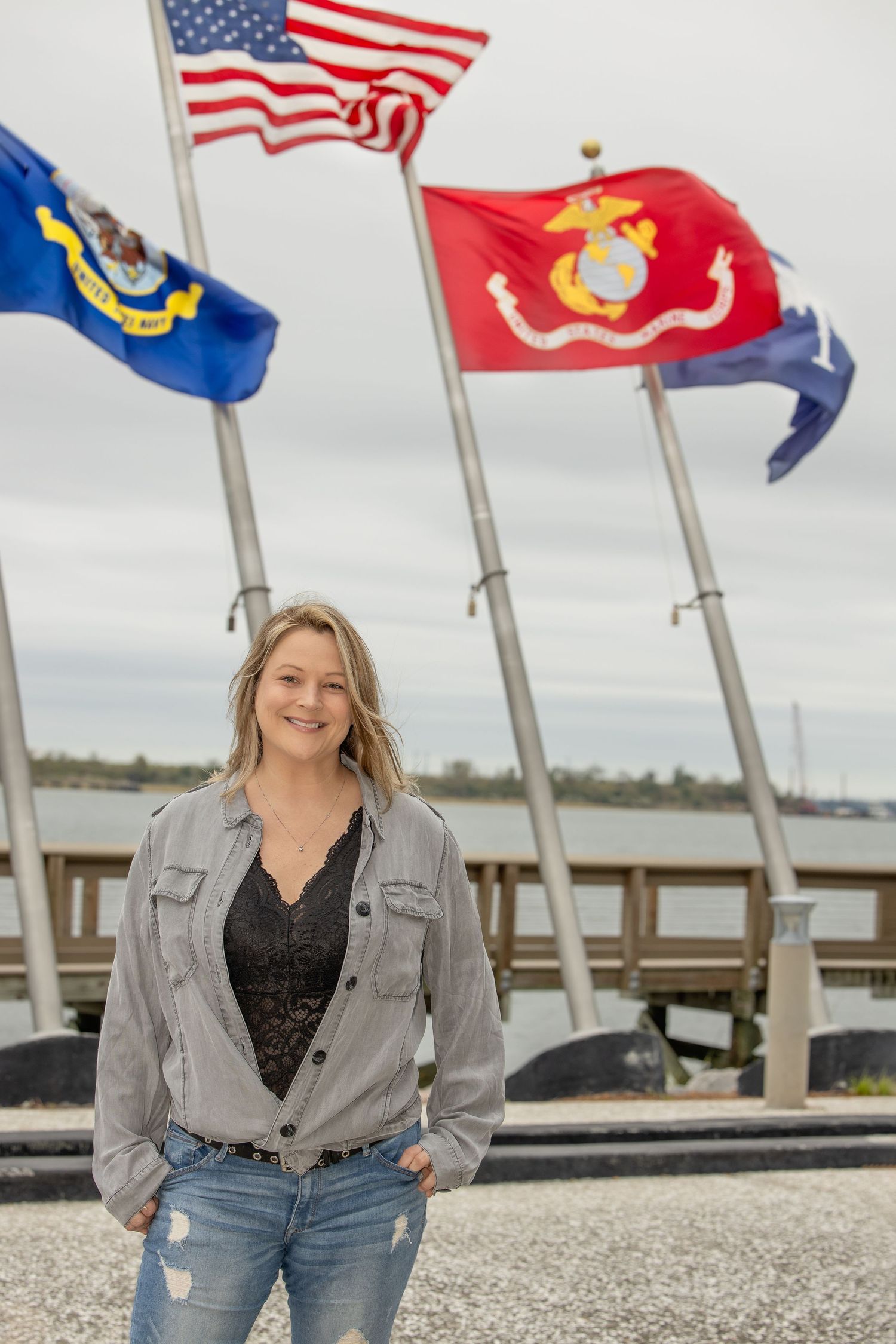 Military flags flying on poles along waterfront boardwalk.