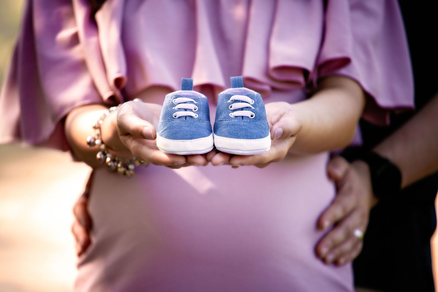 Detail shots of tiny blue baby shoes held against a pink dress background.
