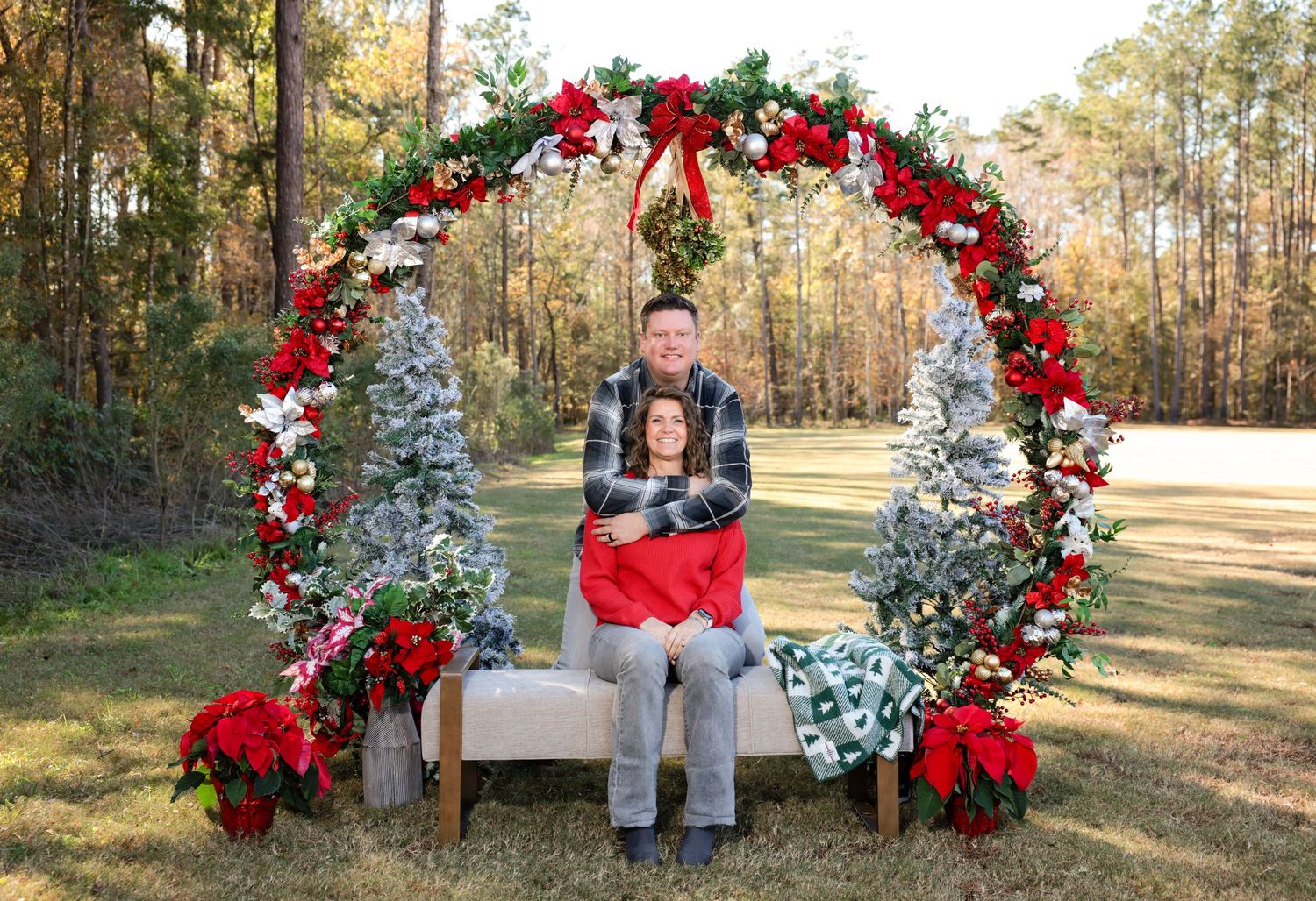 Seasonal family photos under large red and white holiday arch in natural outdoor setting.