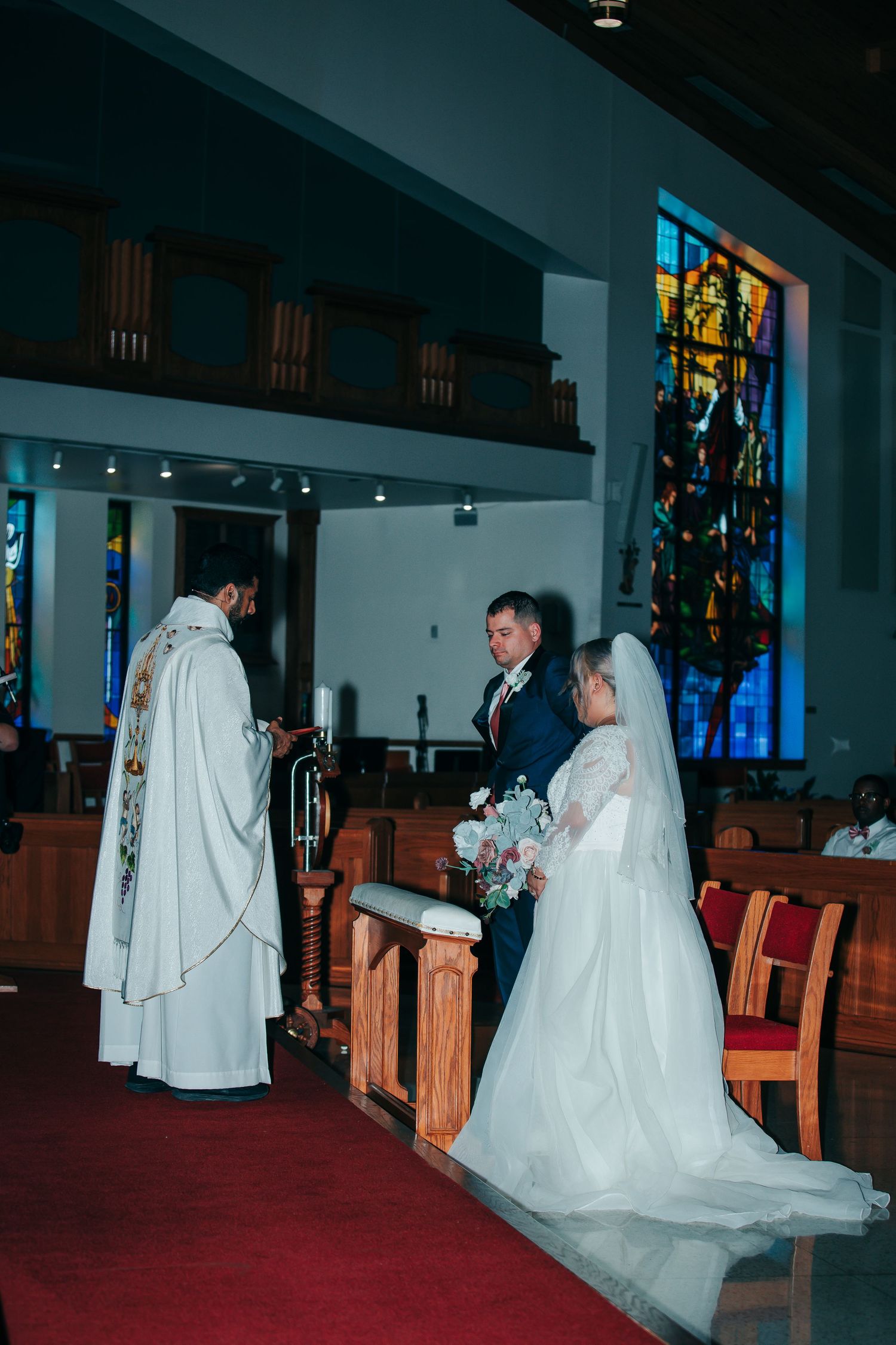 Wedding ceremony in a church with stained glass windows and wooden pews.