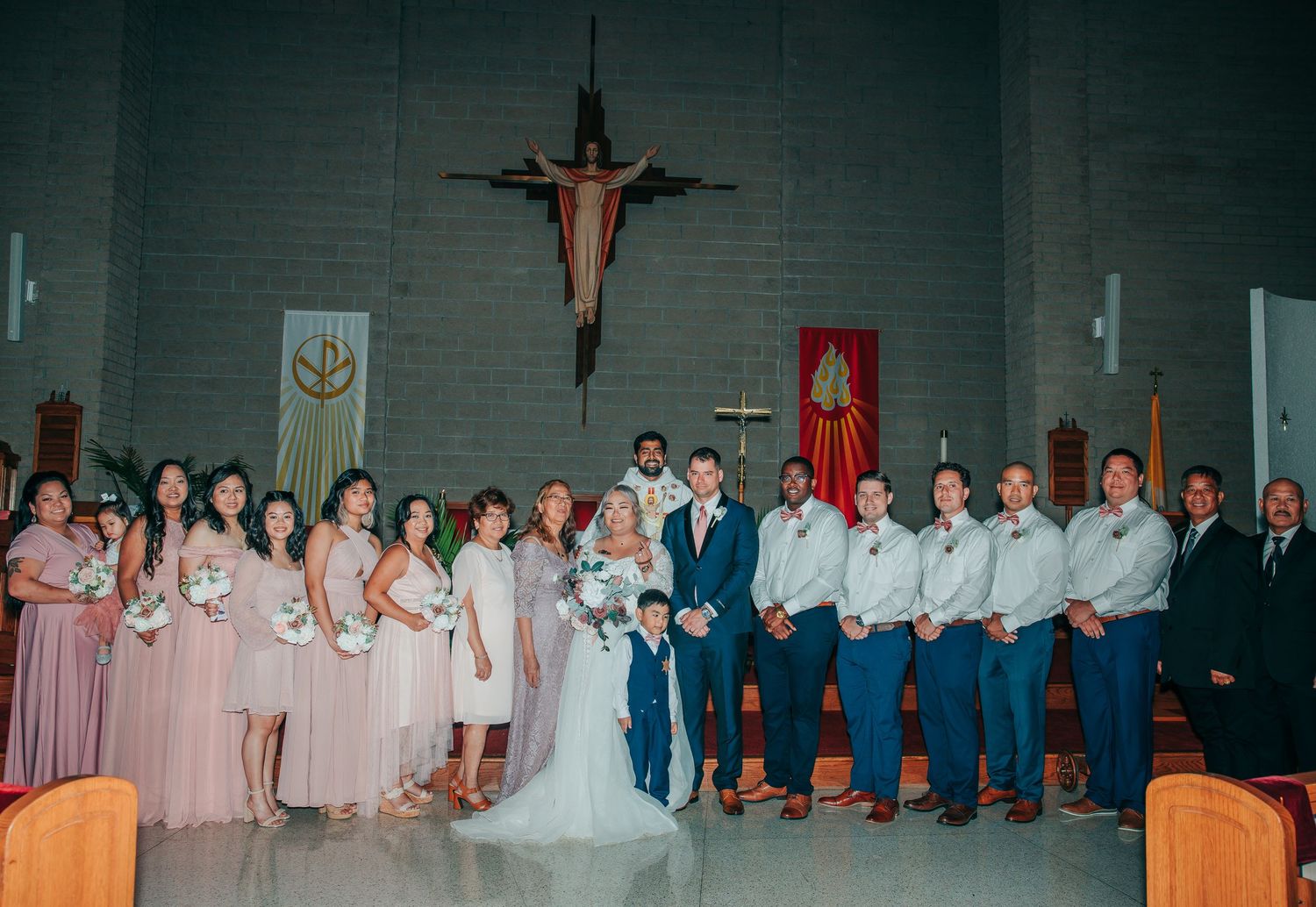 Wedding party lined up in church sanctuary with bridesmaids in pink and groomsmen in dark suits.