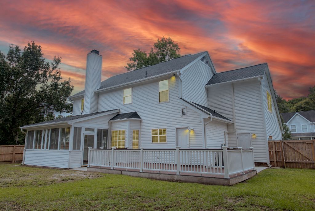 Two-story white house with wraparound porch and deck illuminated at sunset.