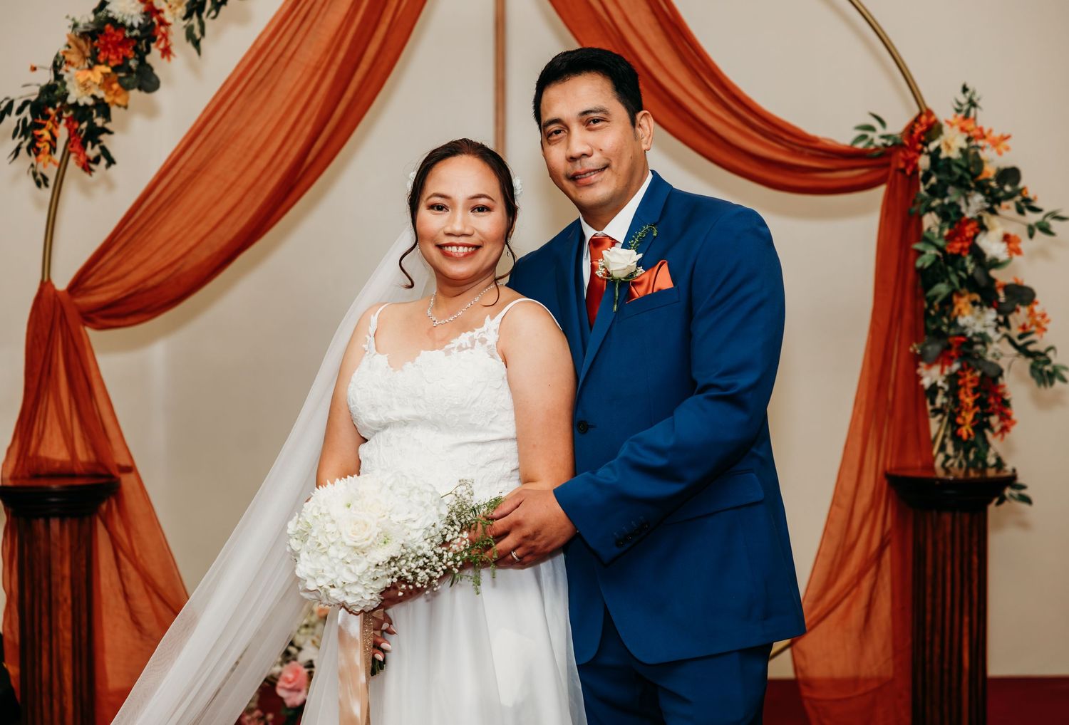 Wedding ceremony exchange under a decorated arch with orange draping and flowers.