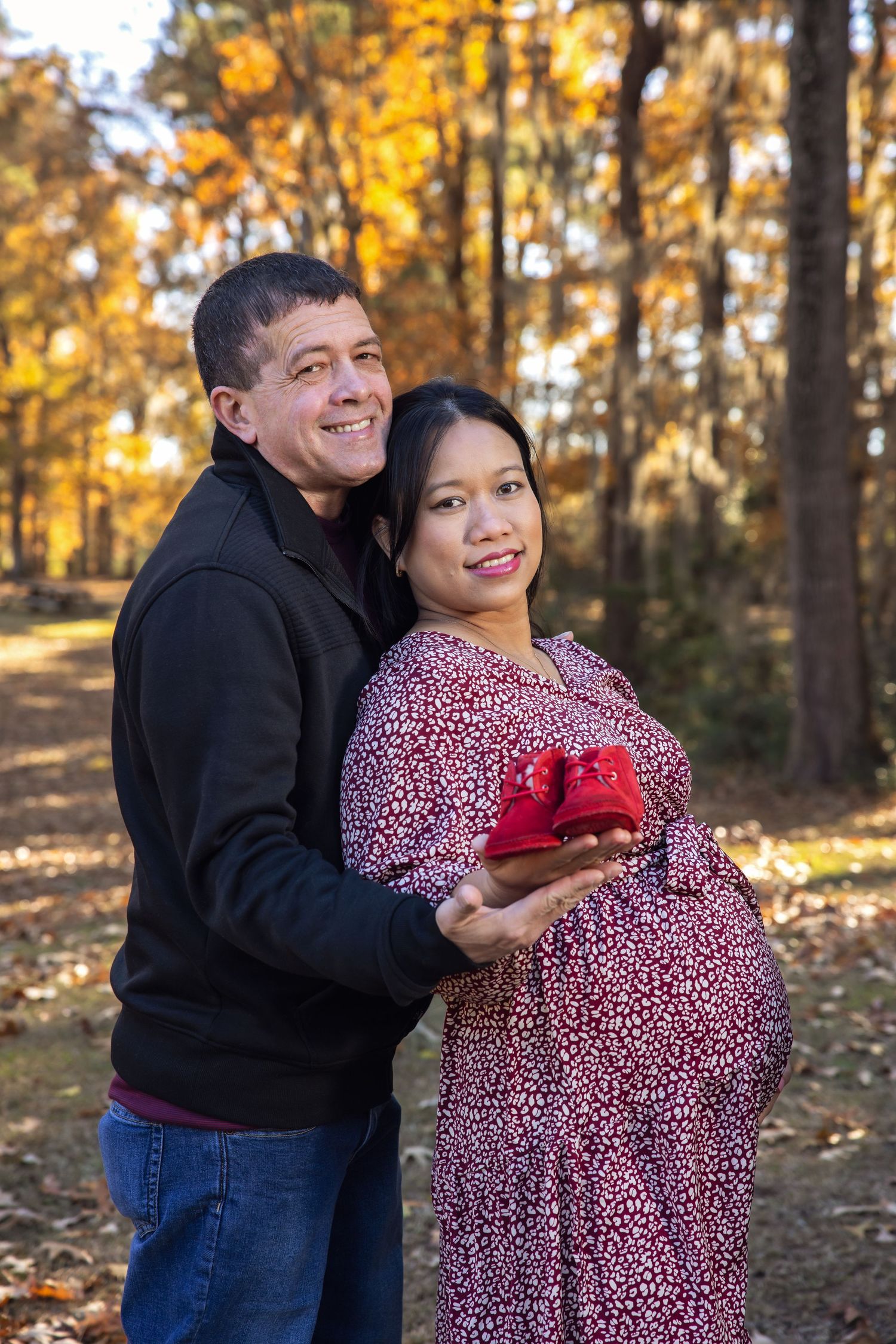 Couple poses with photos during fall engagement session among golden trees.