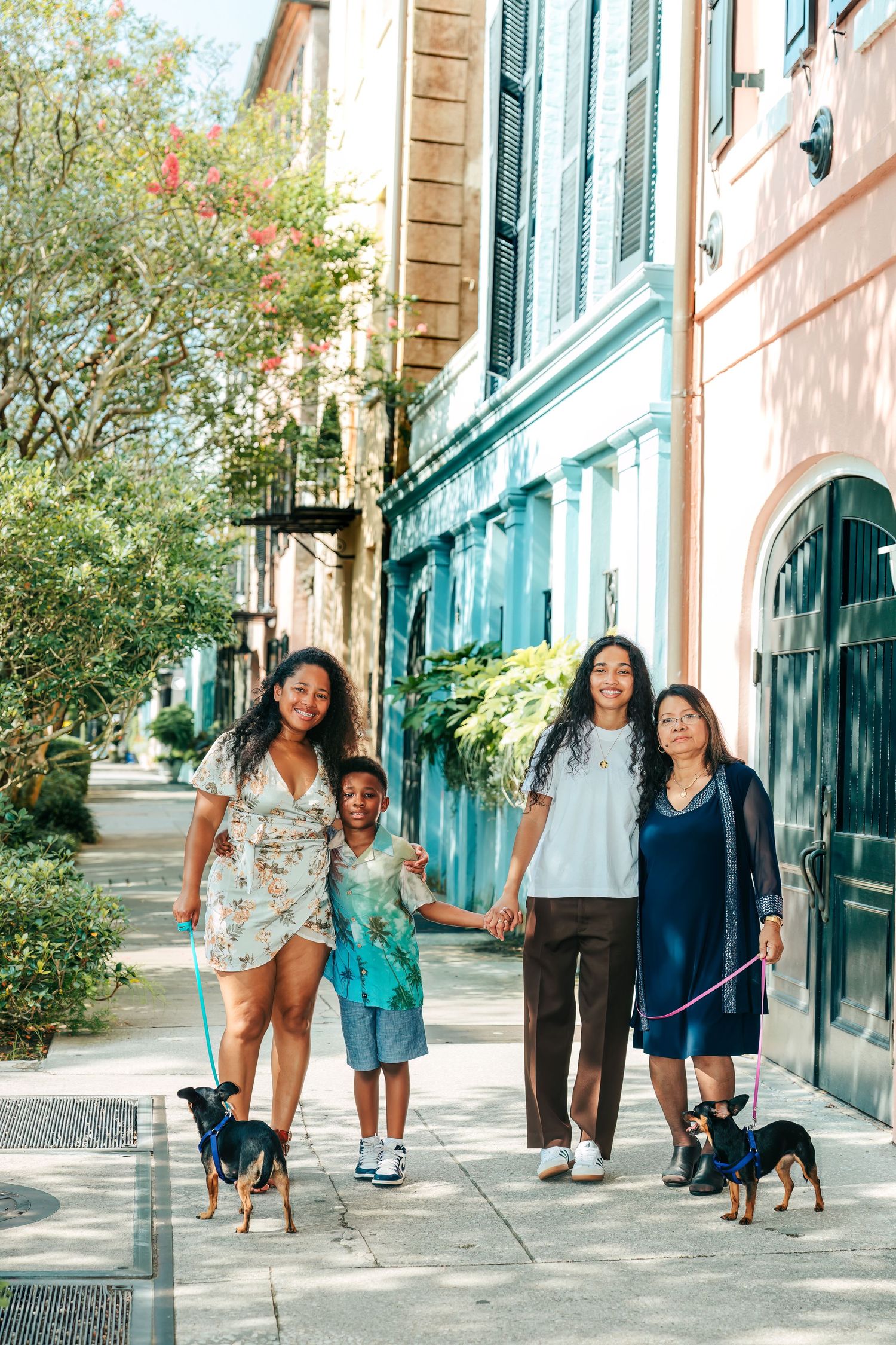 Family walking with dog along pastel colored historic buildings with green shutters.