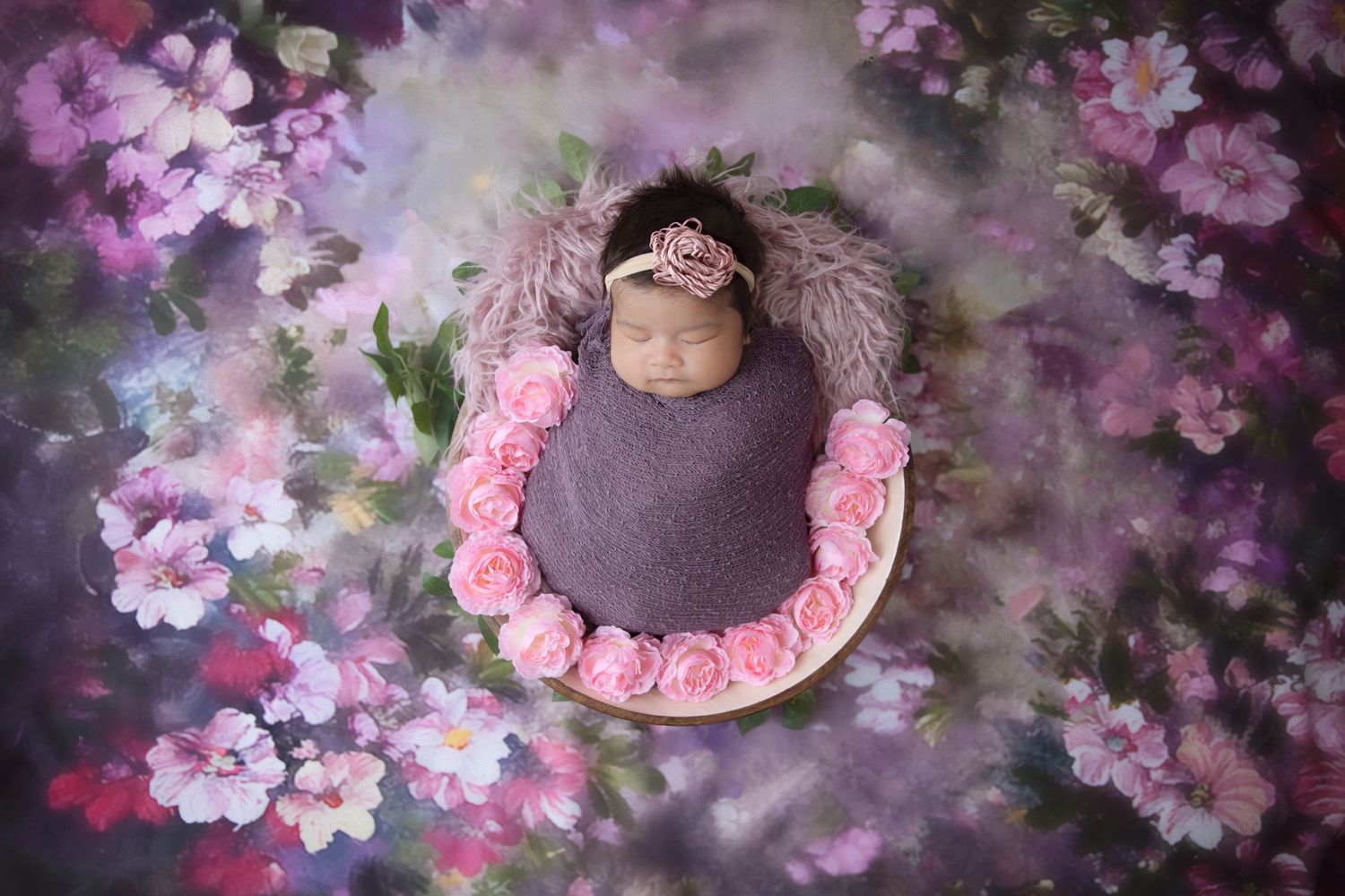 Artistic newborn portrait surrounded by purple and pink floral arrangements.