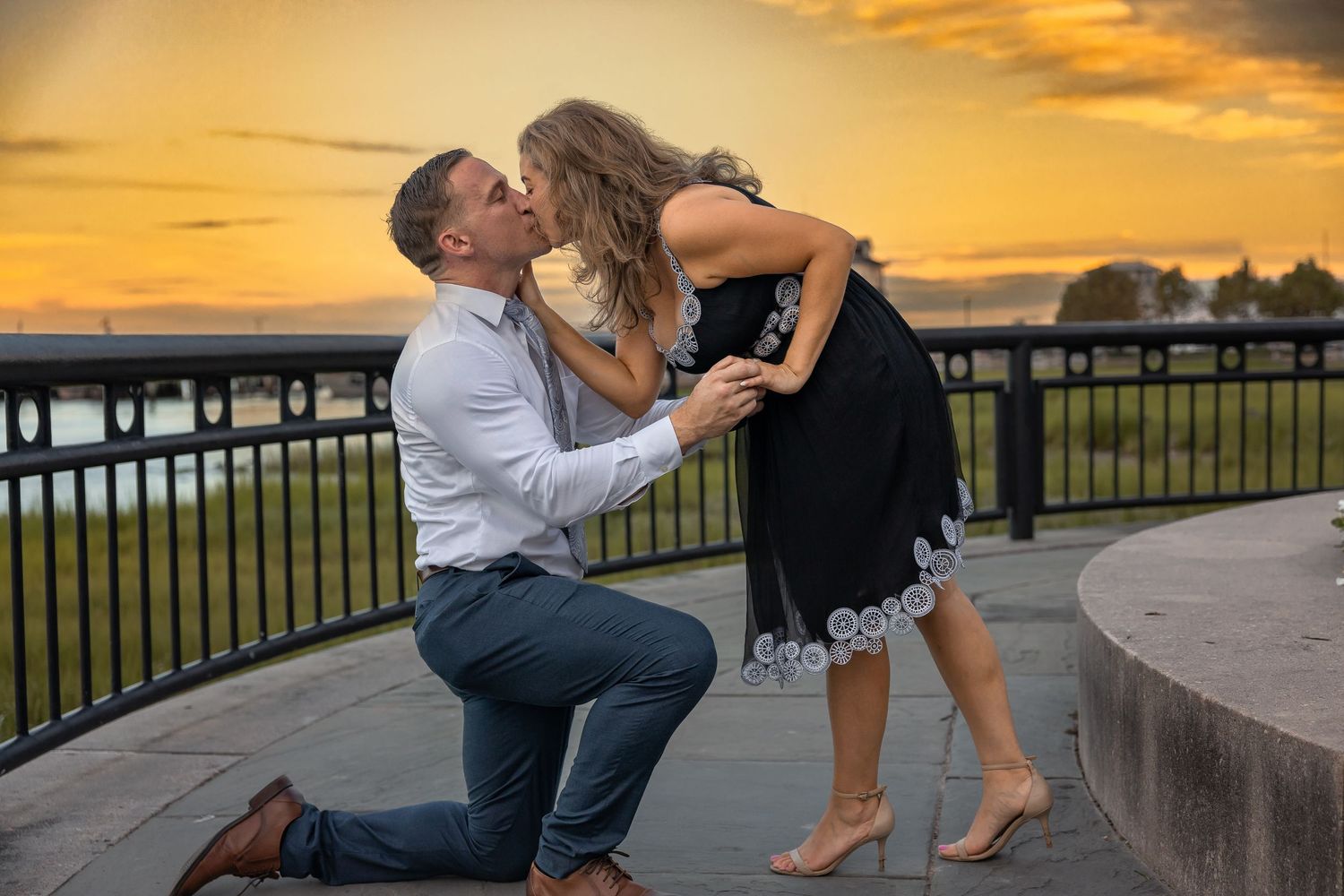 Golden hour engagement session by ornate fountain with dramatic sunset sky.