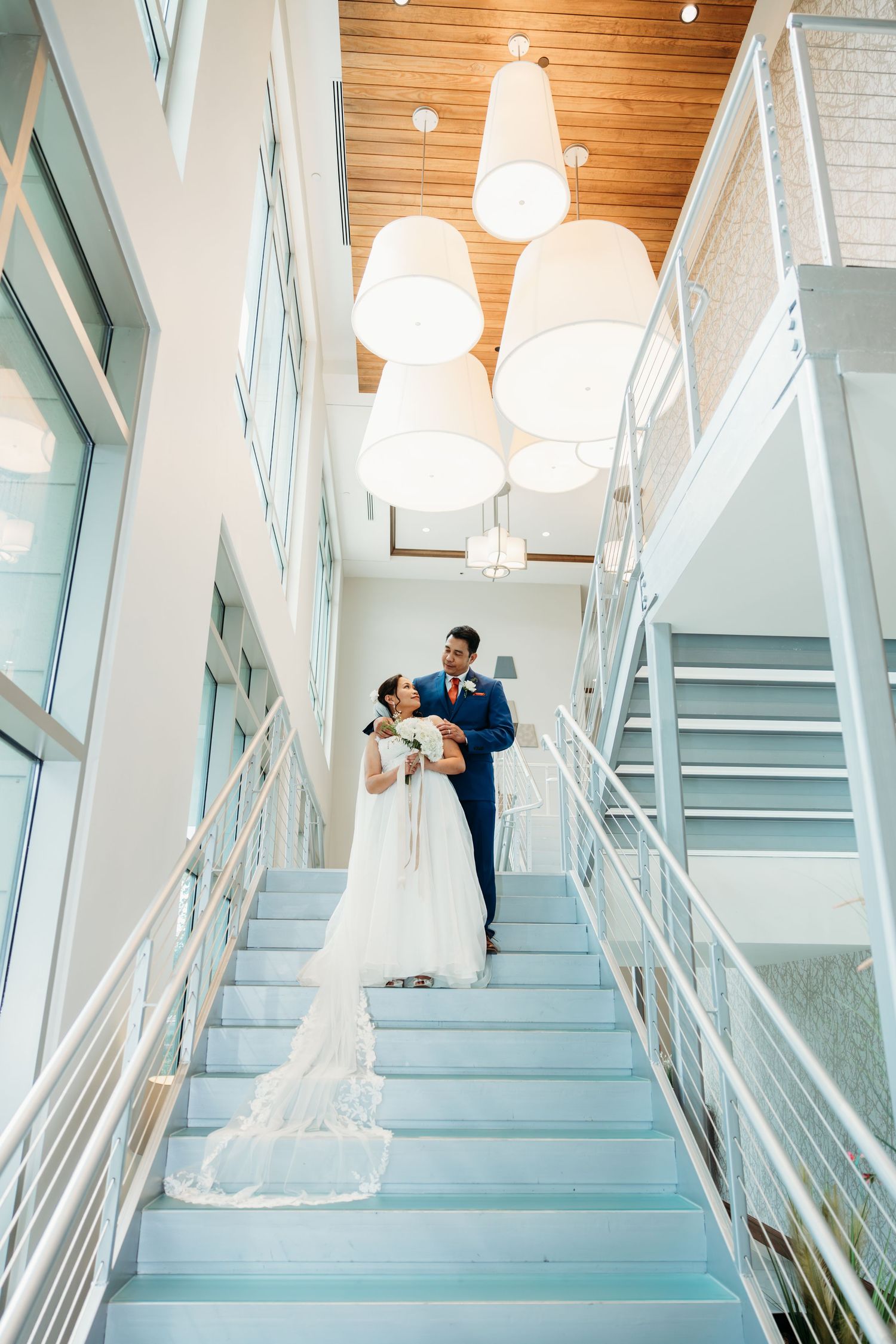 Modern staircase with white railings and pendant lights creates dramatic wedding portrait backdrop.