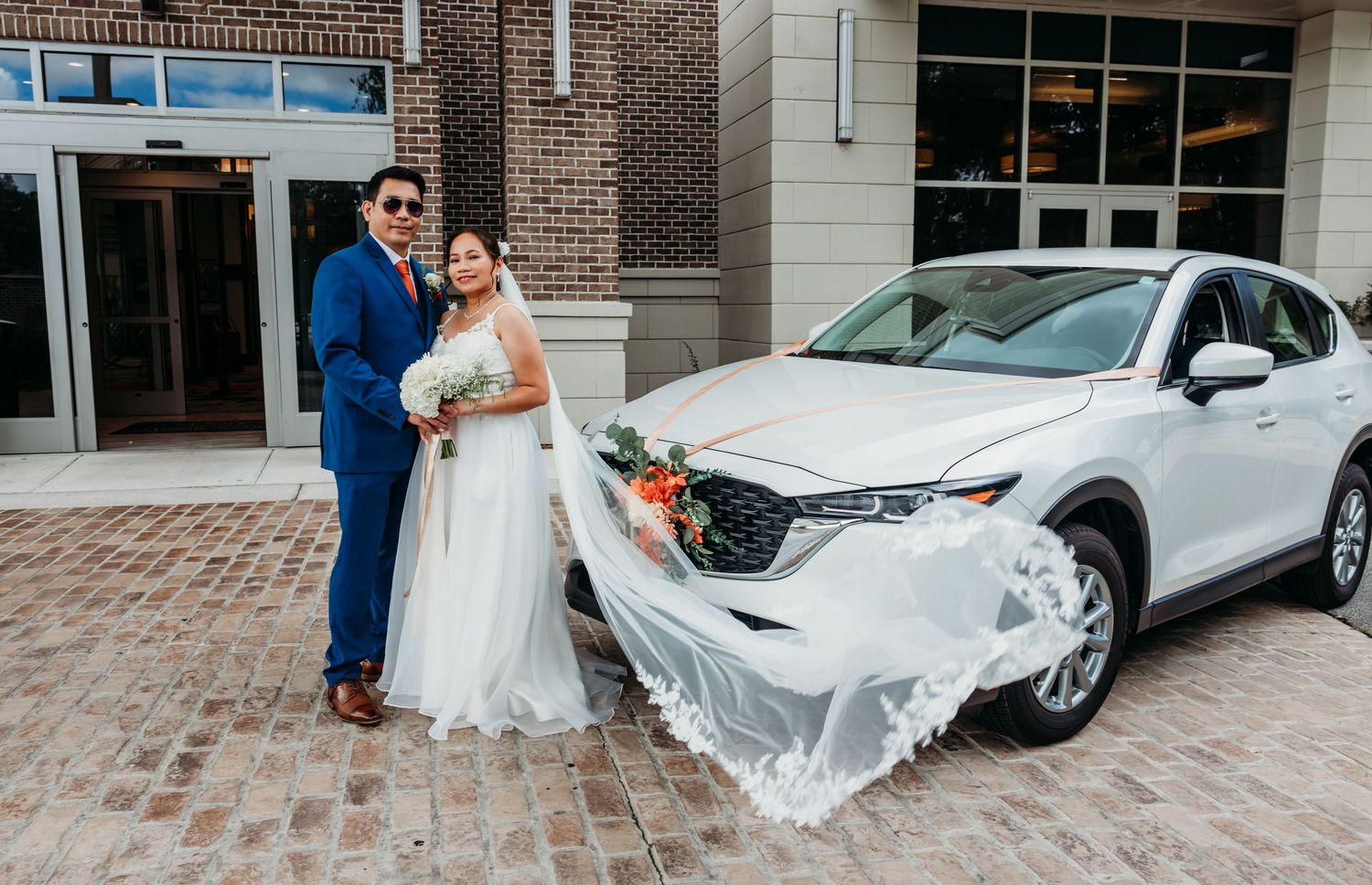 Flowing white wedding dress train billows in the wind outside a brick building.