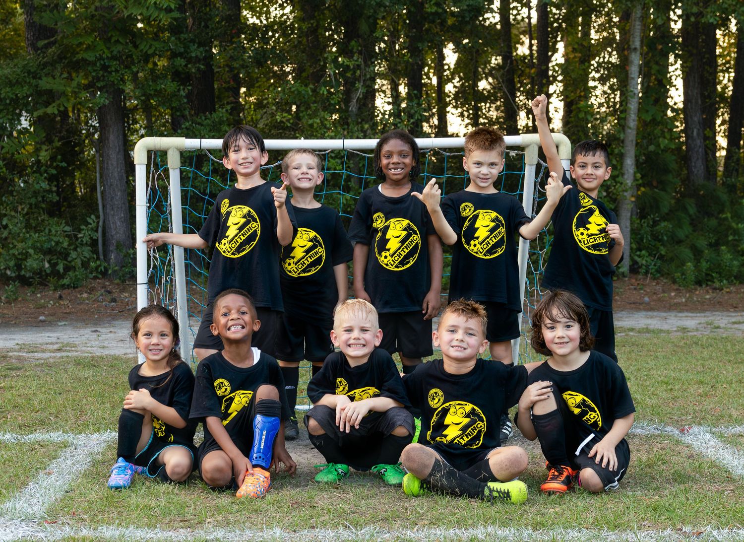 Youth soccer team wearing black and yellow uniforms lined up for a group photo outdoors.